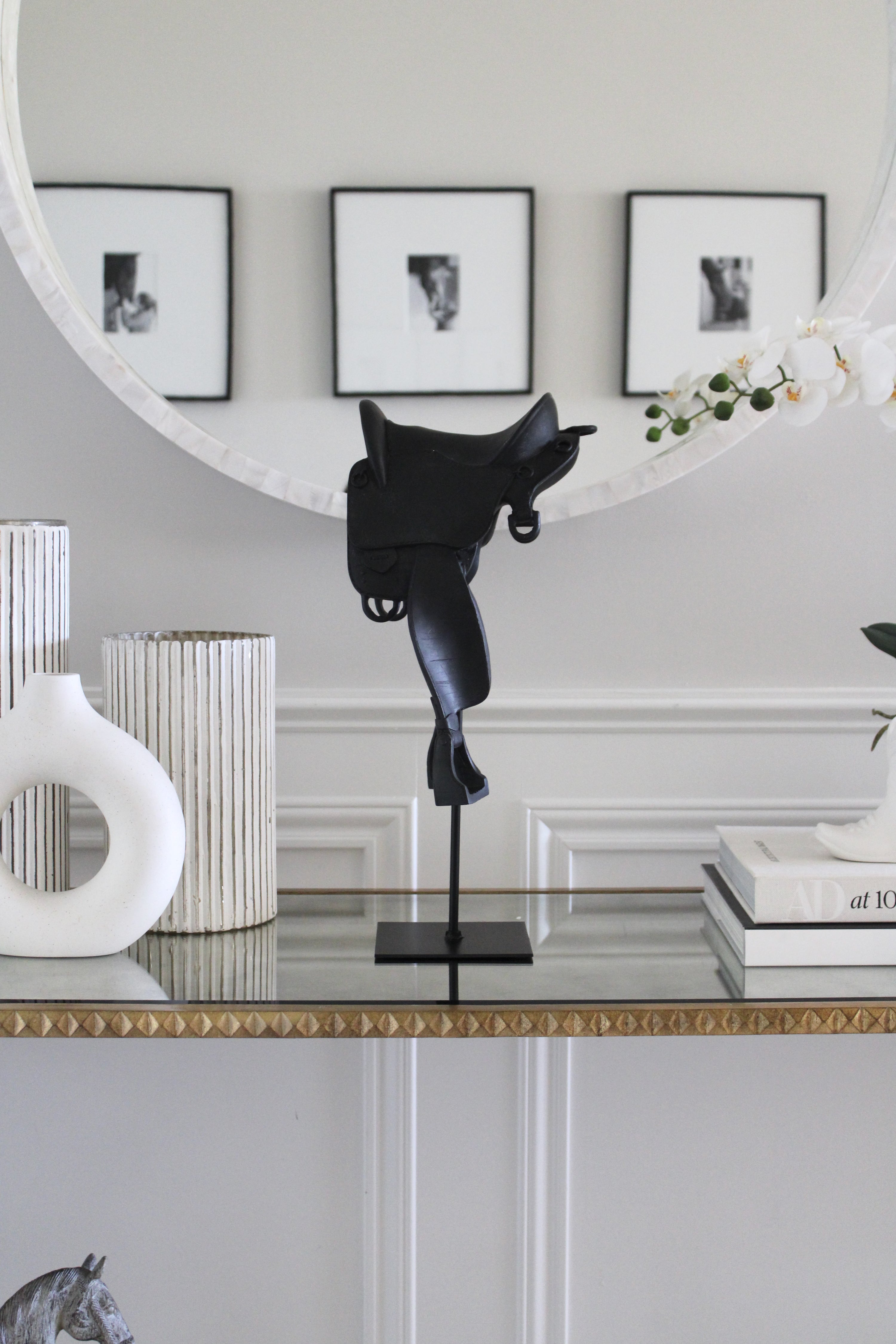 Black English-style horse saddle decor piece crafted from matte-finish resin and metal detailing. Mounted on a black metal stand with a square base, this modern equestrian sculpture captures the elegance of traditional riding saddles and adds a bold statement to home or office décor.