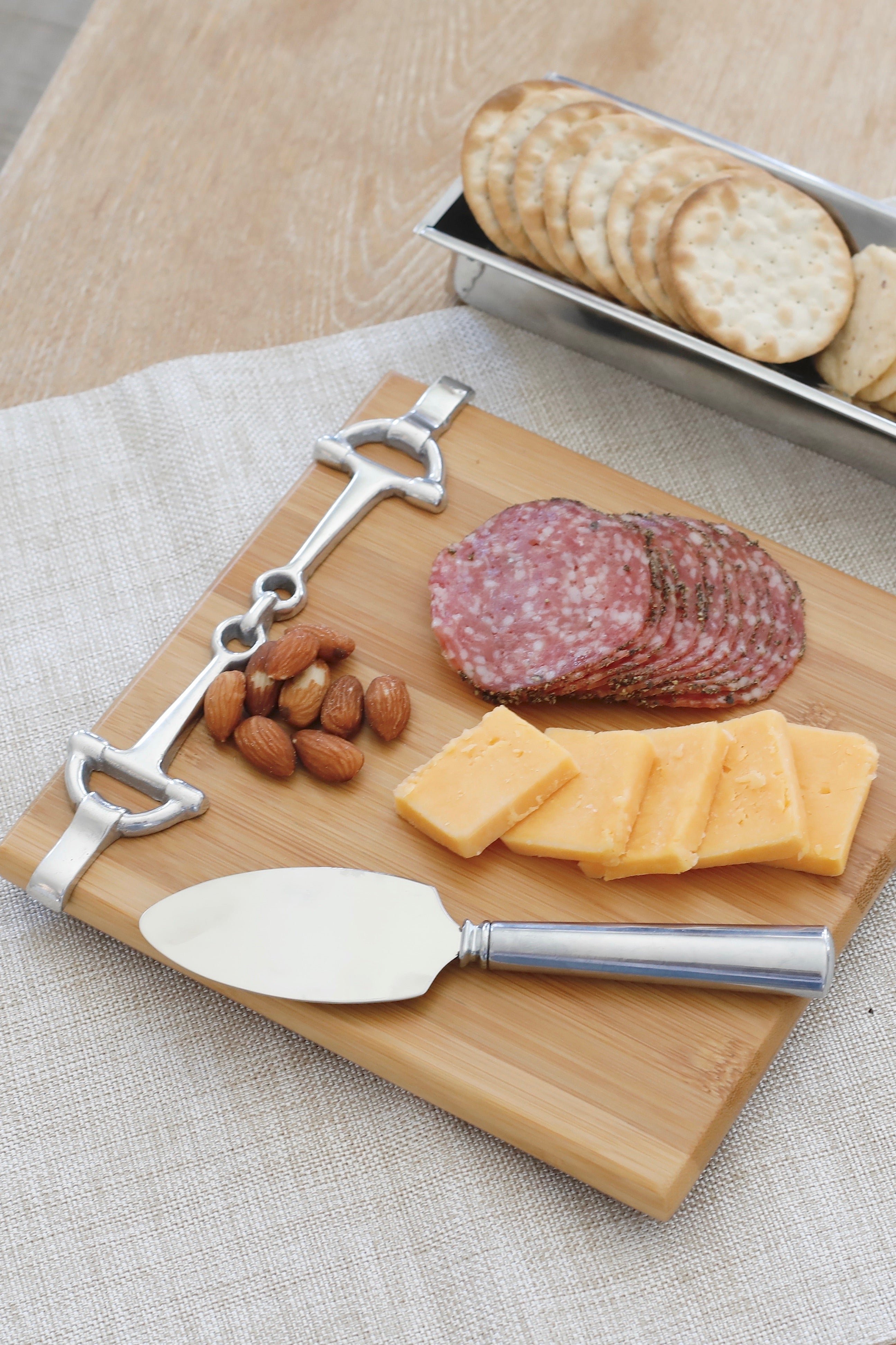 arthur court stylish equestrian well served cheese board snaffle set Well Served Set by Arthur Court featuring a bamboo serving board with a silver alloy horse bit accent, paired with a matching aluminum cheese knife and cracker tray. Elegant equestrian-themed serveware perfect for entertaining or gifting.