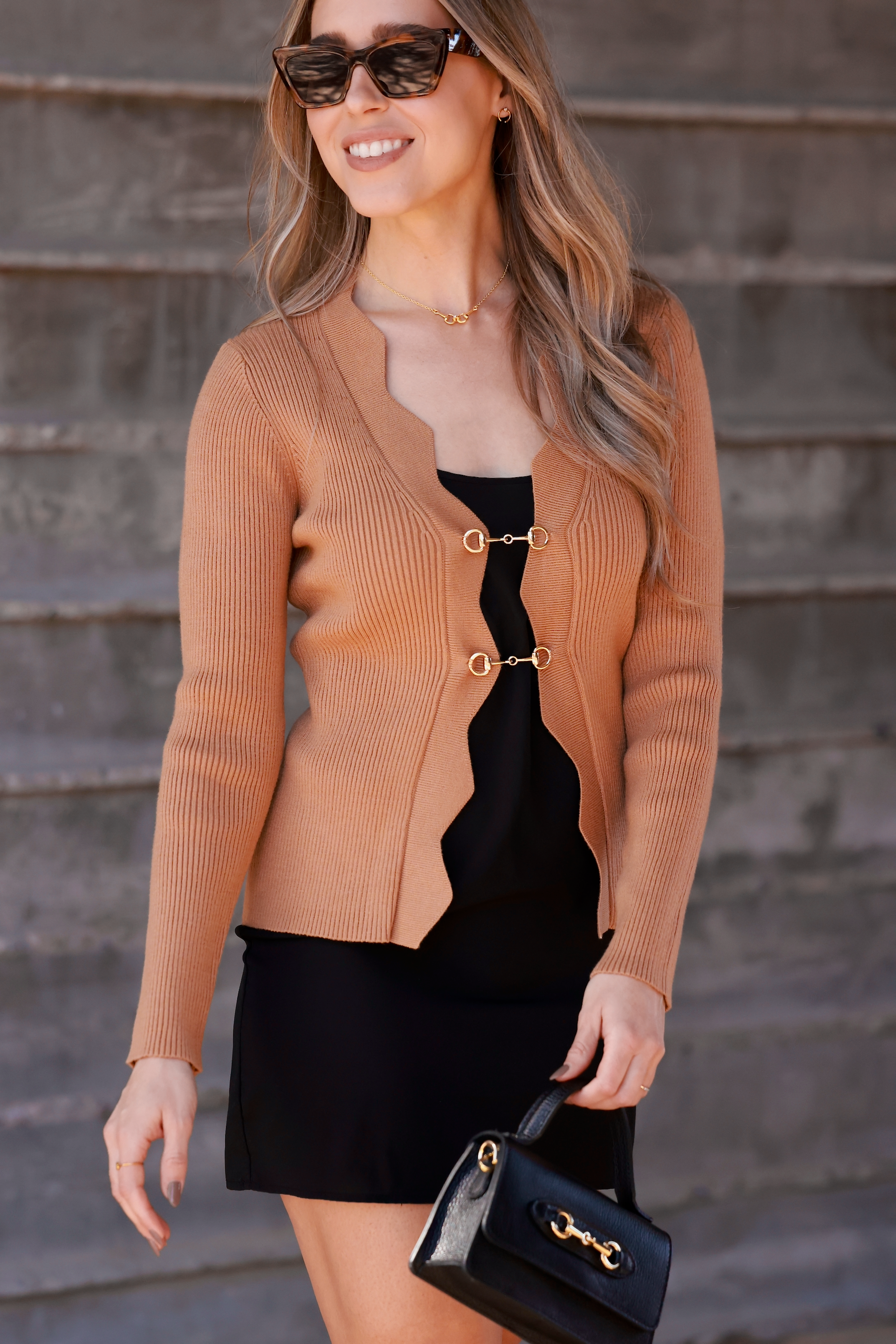 Camel-toned ribbed knit equestrian top featuring a deep scalloped neckline and two gold horsebit closures. Fitted long-sleeve cardigan-style top crafted from a poly/nylon blend, combining timeless elegance with refined equestrian detailing—perfect for fall and winter equestrian fashion.