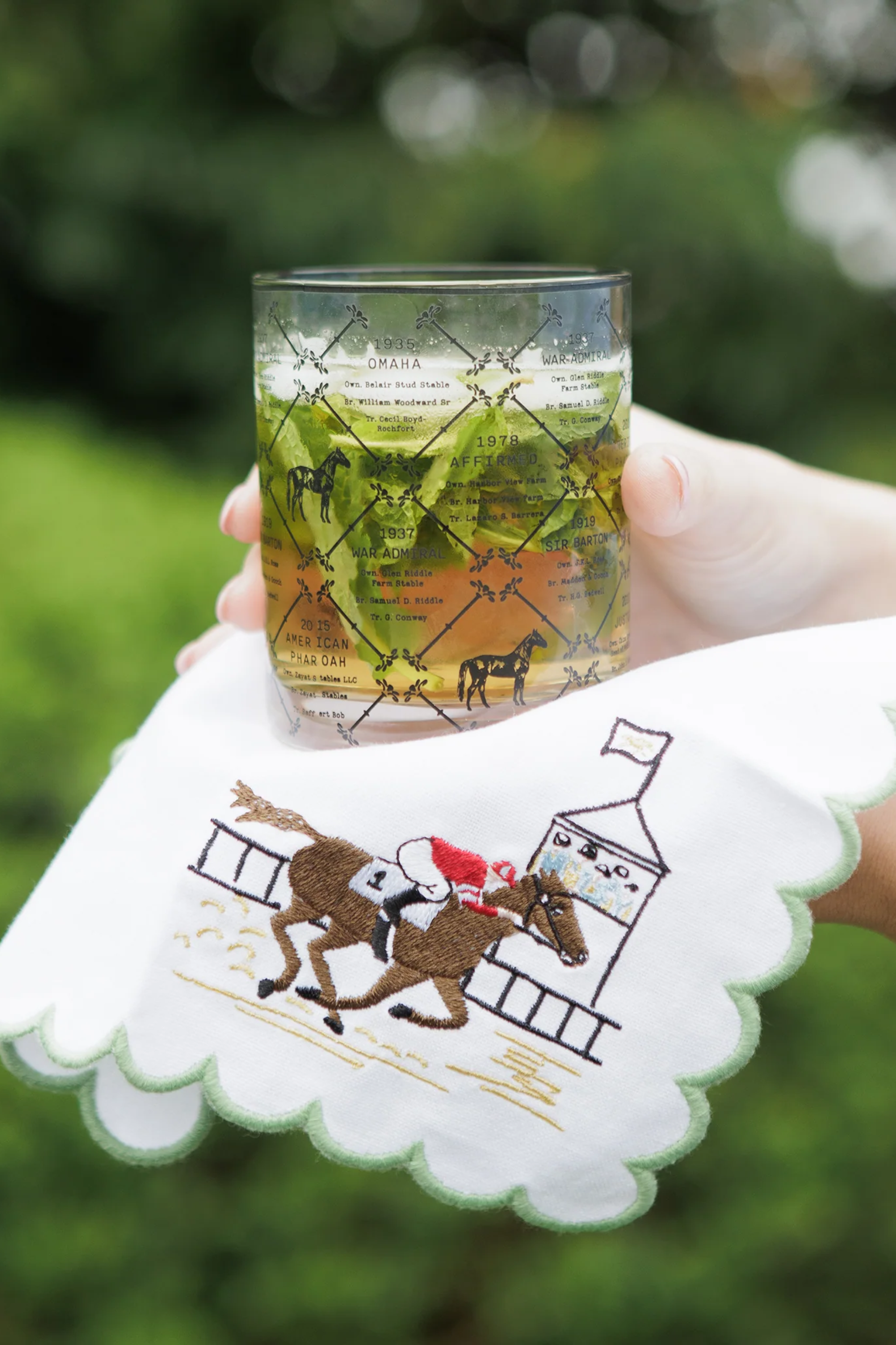 Pomegranate At The Finish Cocktail Napkin Set A toast to the thrill of the track! Our At the Finish Embroidered Cocktail Napkins bring race day excitement to every sip. Featuring a spirited racehorse and jockey charging past the finish line, these embroidered white cotton napkins with a green scalloped edge are a festive nod to the sport of kings—and the queens who throw a fabulous party. 