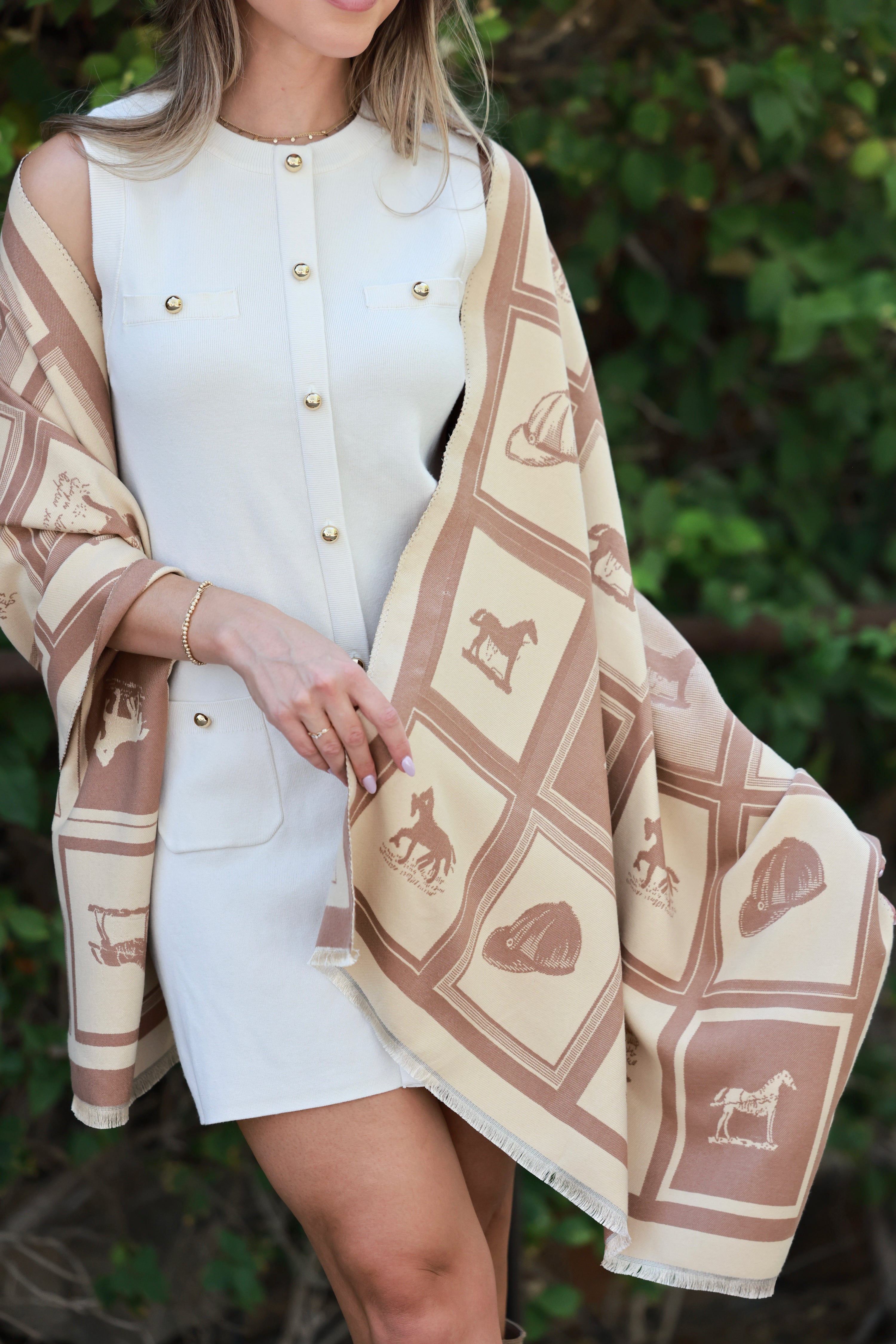 Woman wearing a white dress with a beige patterned shawl over her shoulders against a green background - horse motif scarf, equestrian inspired shawl, horse girl wrap, equestrian blanket scarf, designer inspired horse themed accessory, horse show accessory