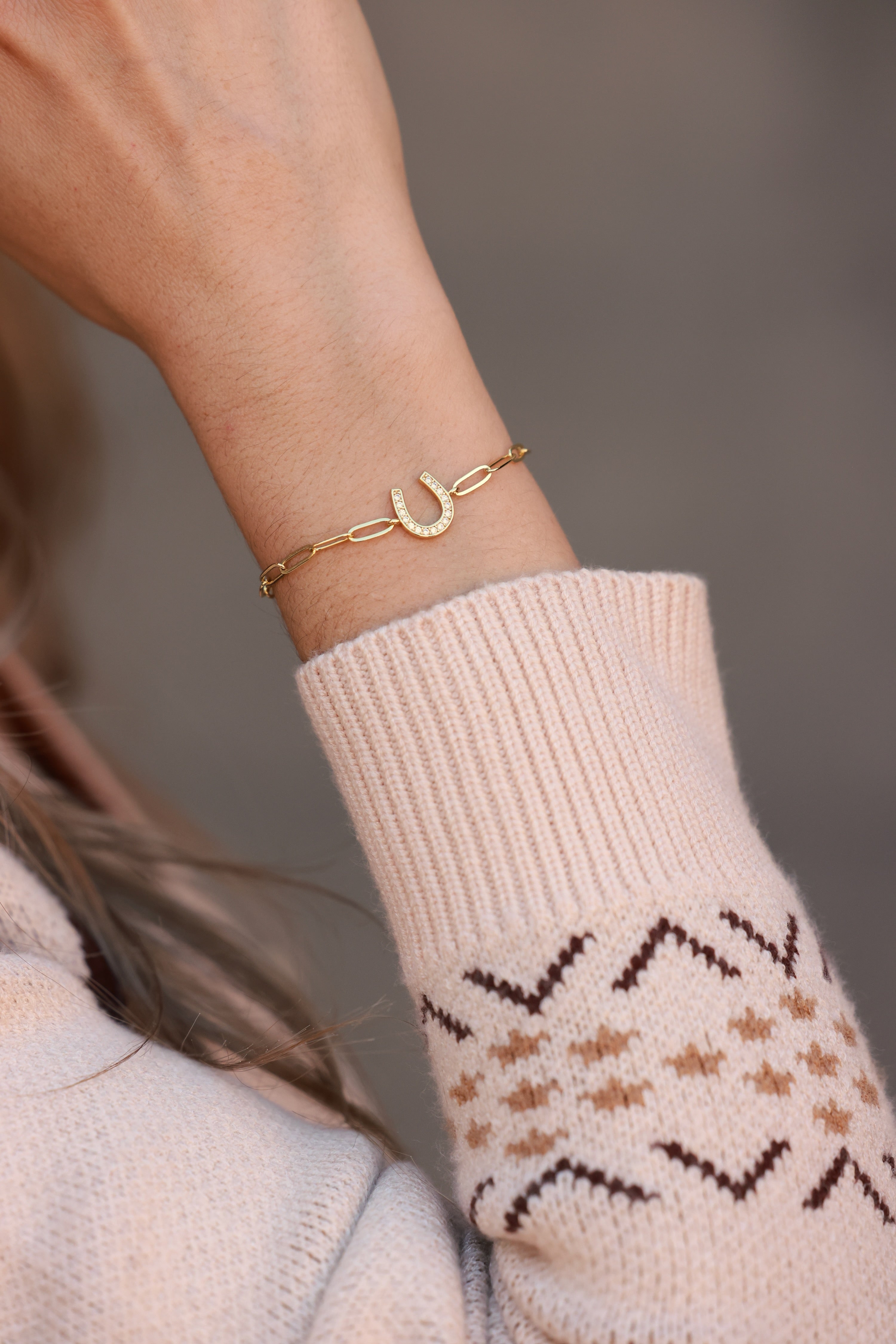 Gold bracelet with a horseshoe charm on a person's wrist, wearing a beige outfit. - equestrian inspired jewelry, horse girl accessory, horseshoe bracelet, dainty equestrian jewelry, meaningful gifts for horse lover