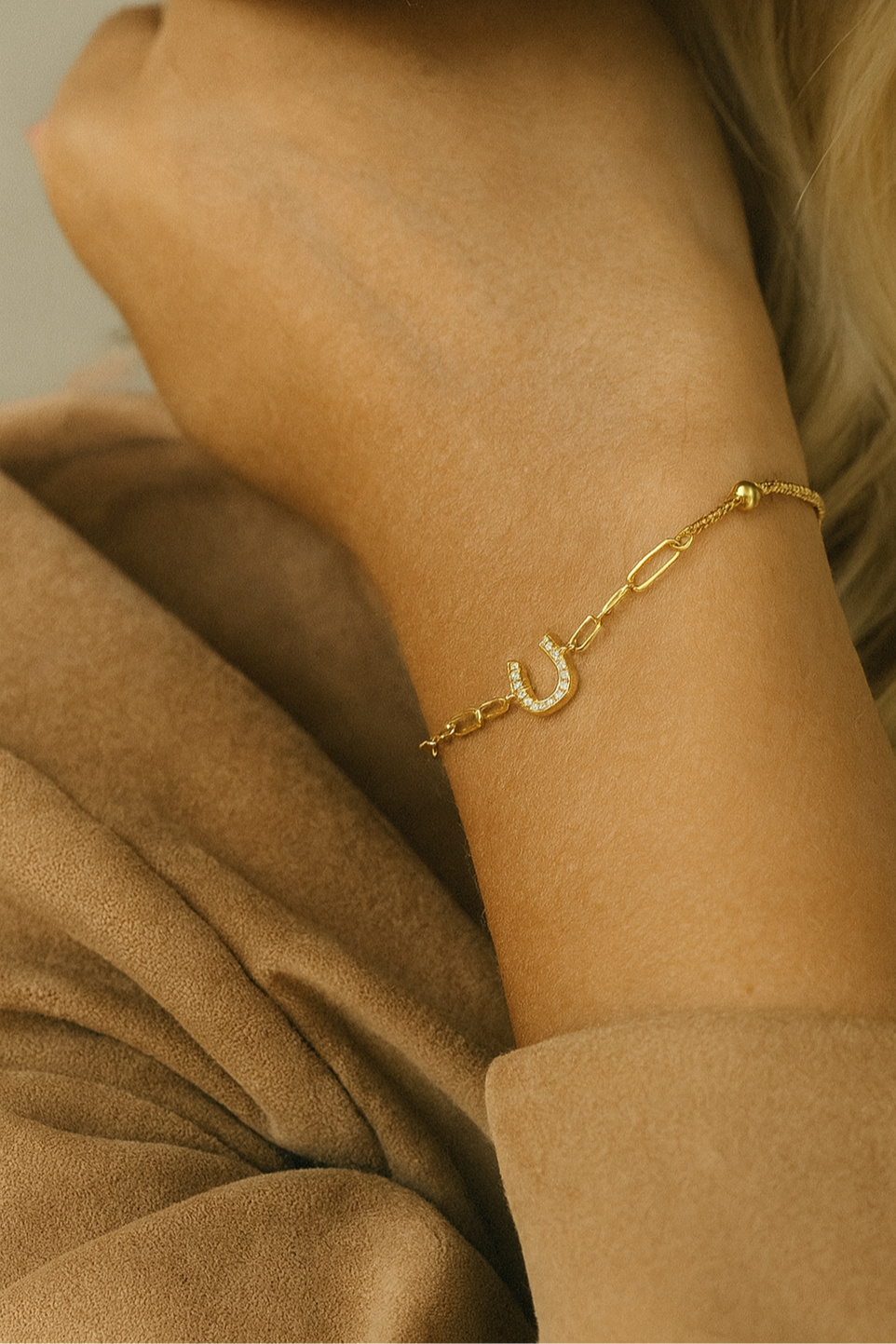 Gold bracelet with a horseshoe charm on a person's wrist, wearing a beige outfit. - equestrian inspired jewelry, horse girl accessory, horseshoe bracelet, dainty equestrian jewelry, meaningful gifts for horse lover