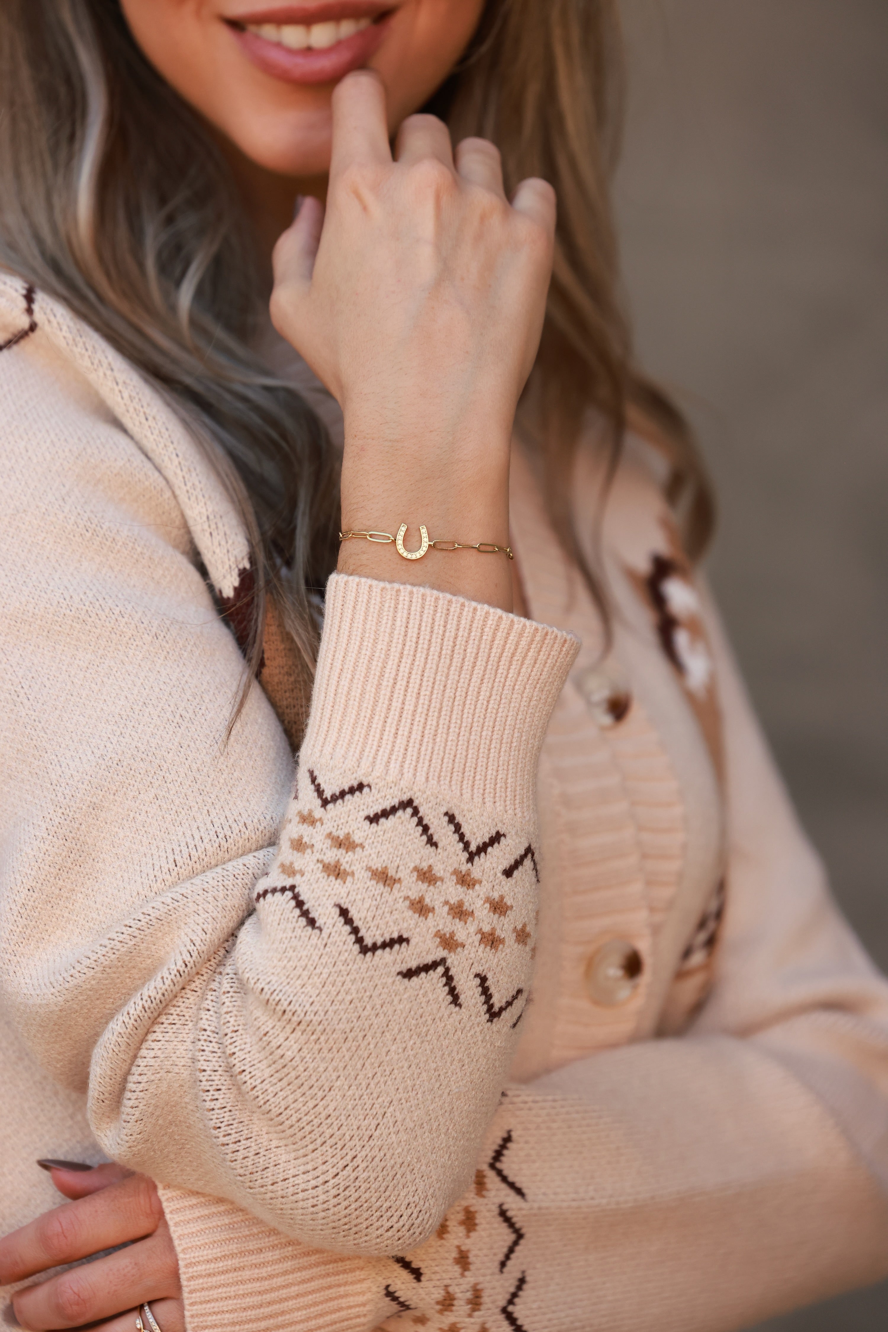 Gold bracelet with a horseshoe charm on a person's wrist, wearing a beige outfit. - equestrian inspired jewelry, horse girl accessory, horseshoe bracelet, dainty equestrian jewelry, meaningful gifts for horse lover