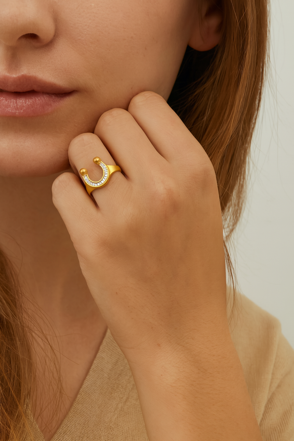 Close-up of a hand wearing a gold ring with a crescent moon design, touching the face.