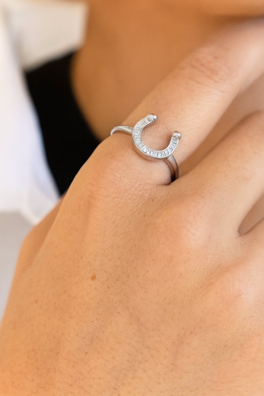 Silver horseshoe ring on a person's finger with a blurred background