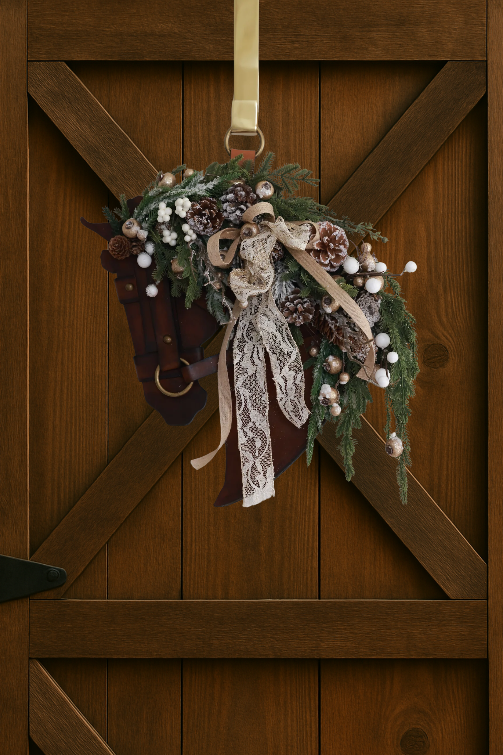 A handcrafted equestrian holiday wreath featuring a sculpted genuine leather horse profile adorned with winter greenery, frosted pinecones, pearl-accented berries, shimmering metallic details, and a layered lace and linen bow. The wreath measures approximately 16 inches by 12 inches and is designed for indoor or outdoor display.