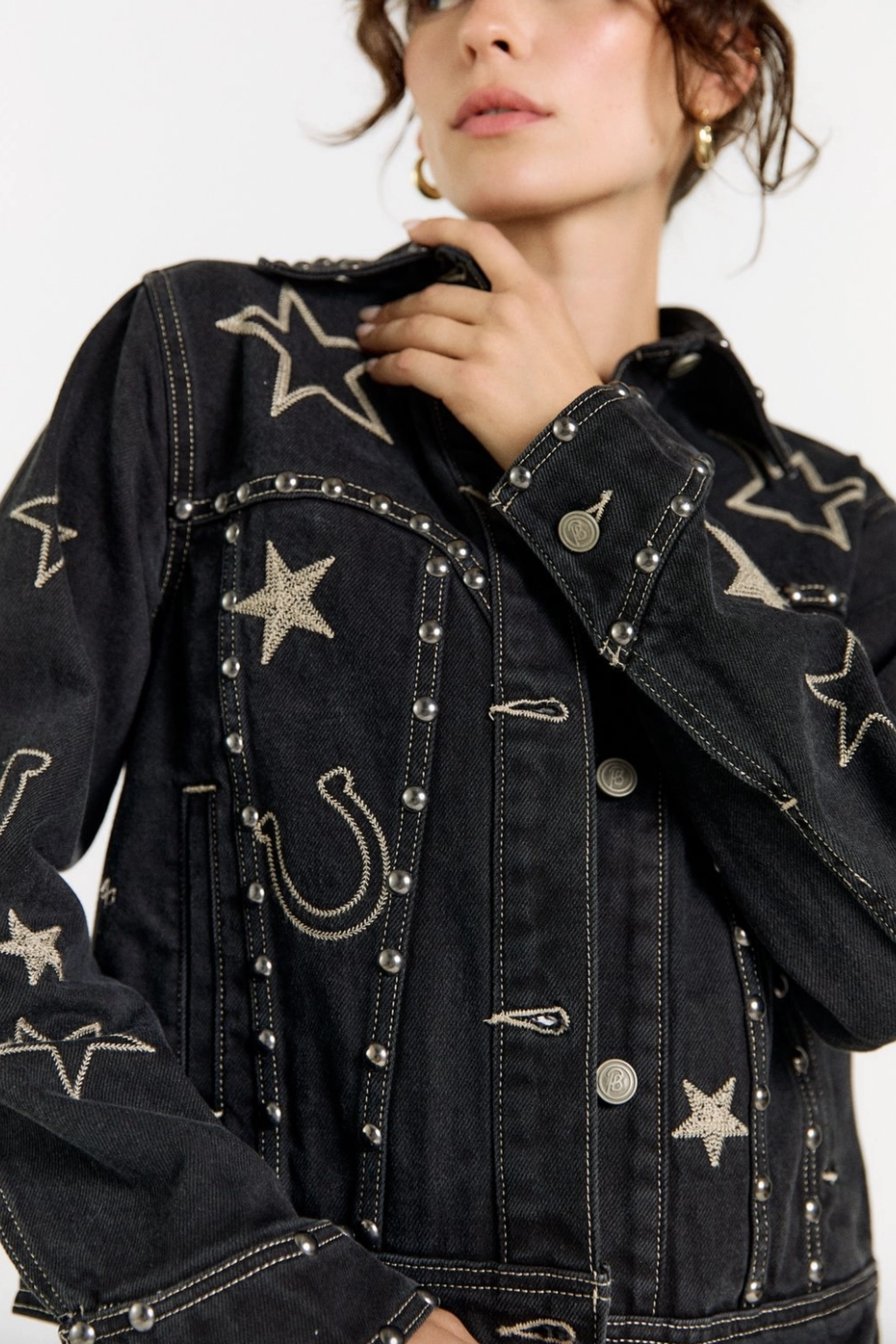 Black cotton denim jacket with all-over equestrian and western-inspired embroidery, including horseshoes and stars, accented with metallic rivet detailing.