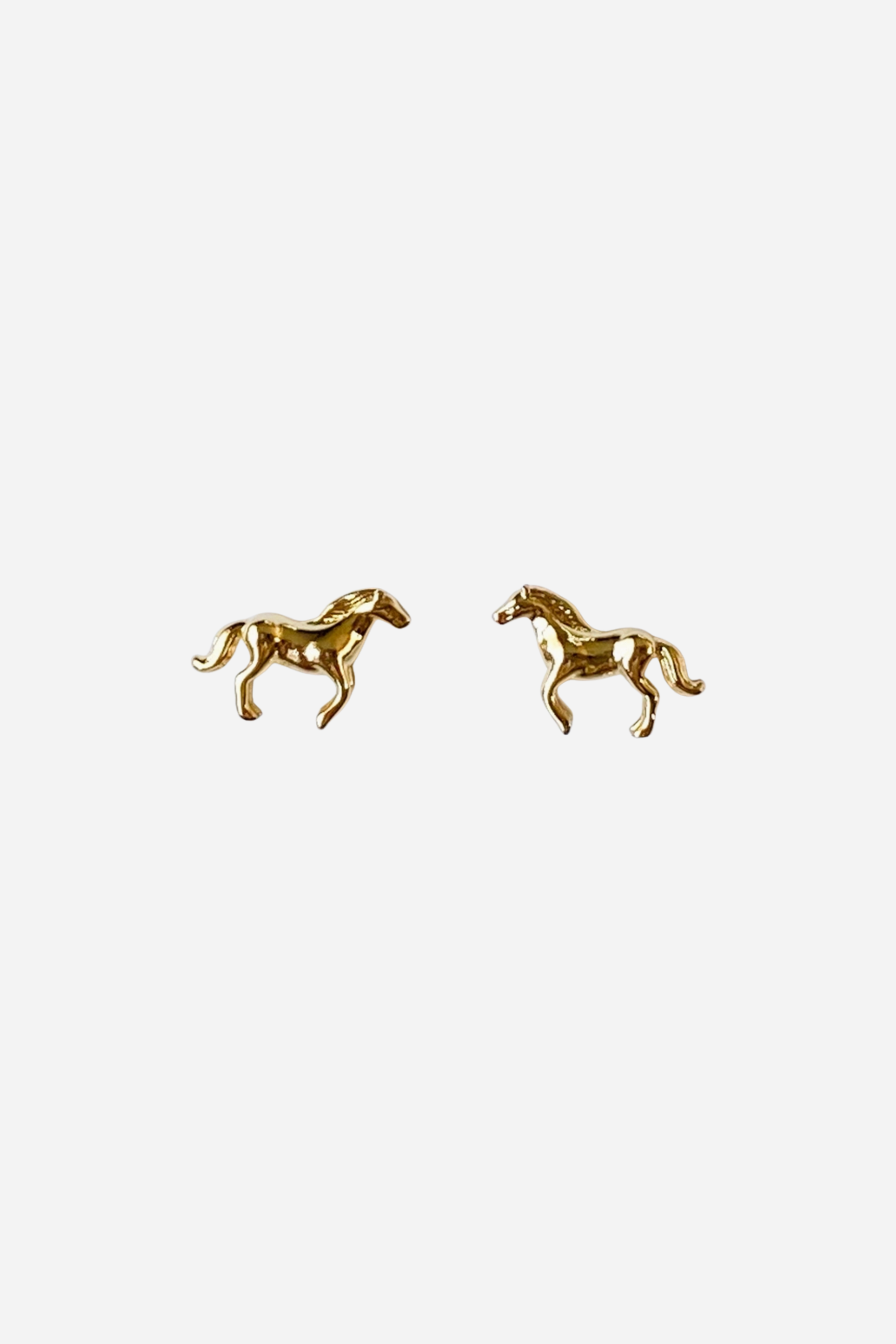 Pair of dainty gold horse-shaped stud earrings displayed on a white background, their detailed mane and tail catching the light for an elegant look. Made with 14K gold plating and nickel-free, perfect for horse lovers and equestrian enthusiasts.