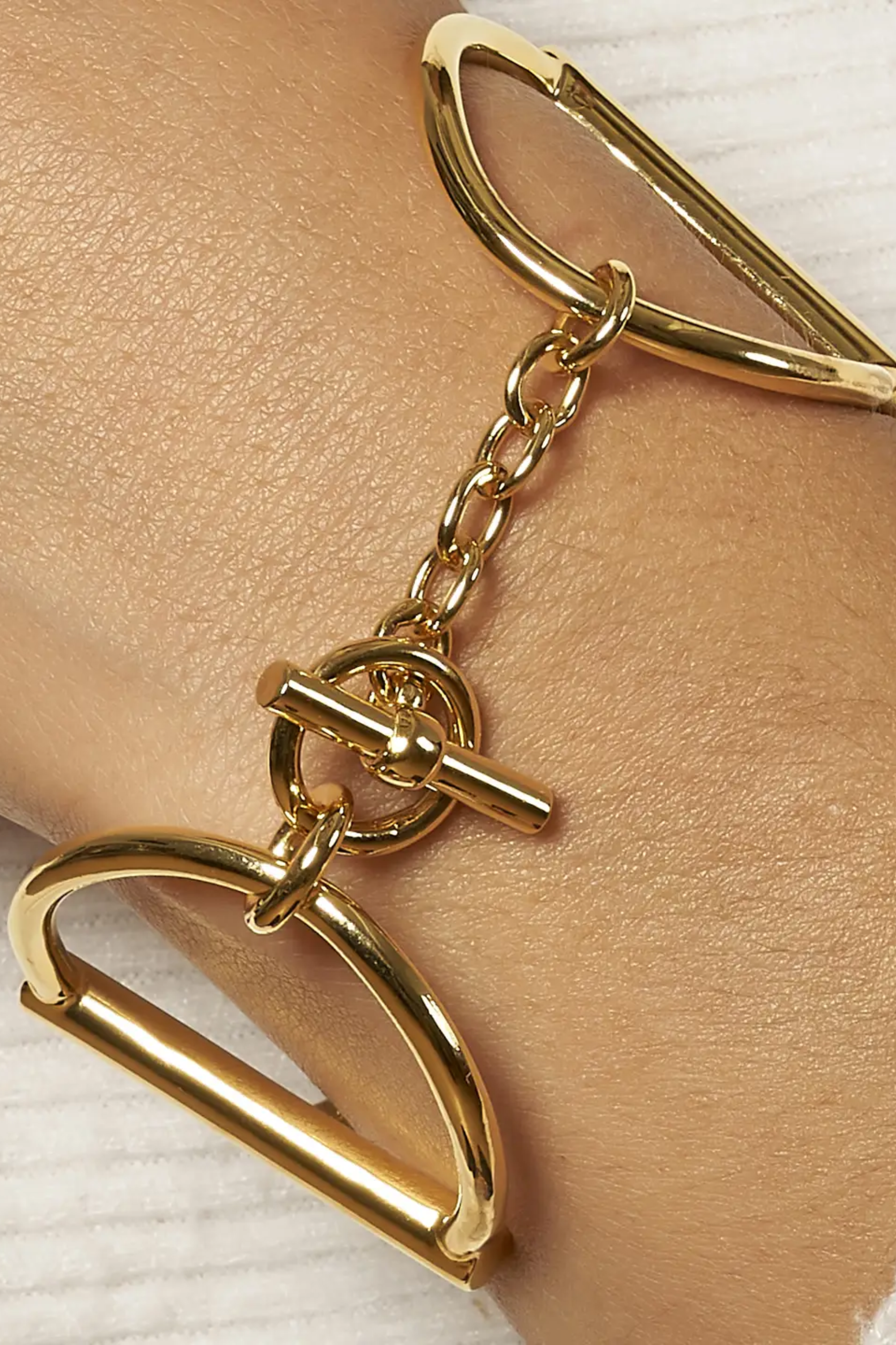 Heritage Horse Bit Gold Cuff — a bold, polished gold-over-brass bracelet with a sleek, modern open-triangle design, 1½-inch width, and iconic double horse-bit motif, connected by small links and secured with a signature toggle-and-ring clasp, elegantly curved to fit a 7½-inch wrist, photographed on a white background.