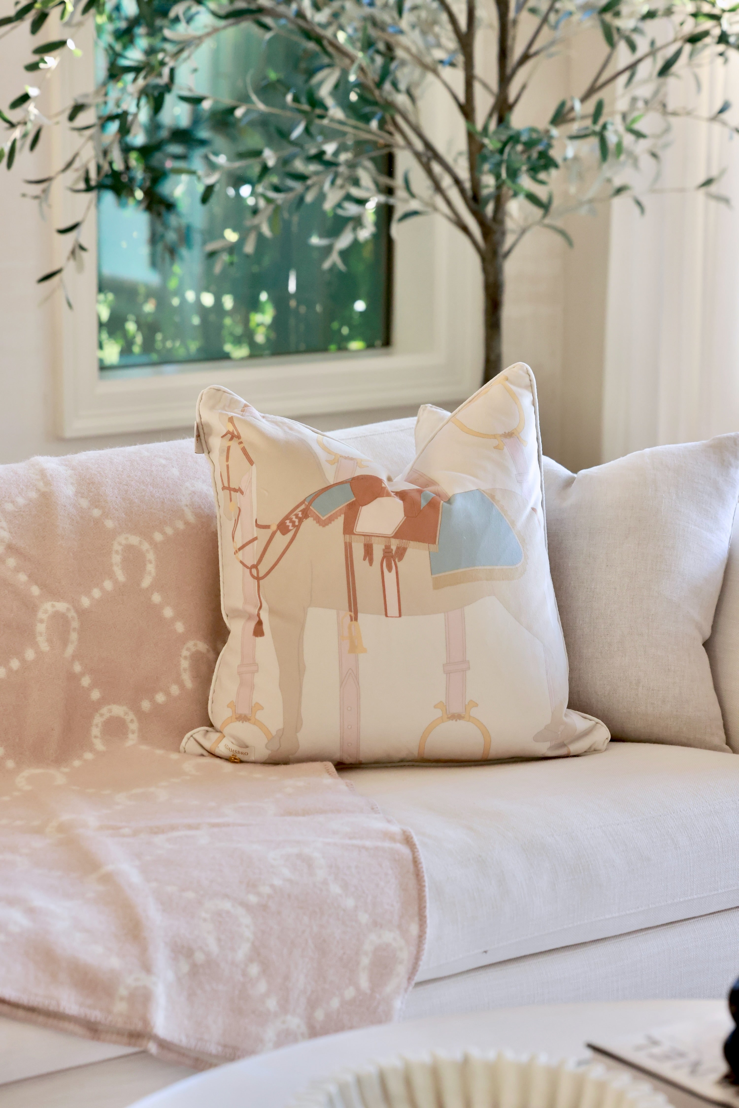 Heritage Horse pastel velvet pillow with equestrian-inspired design, luxury home décor cushion in off-white and beige tones, soft feather-filled insert, perfect for living rooms, bedrooms, or tack rooms. Decorative pillow with a soft brown horse design, featuring a blue and brown saddle. The background is light beige with subtle equestrian-themed accents. 