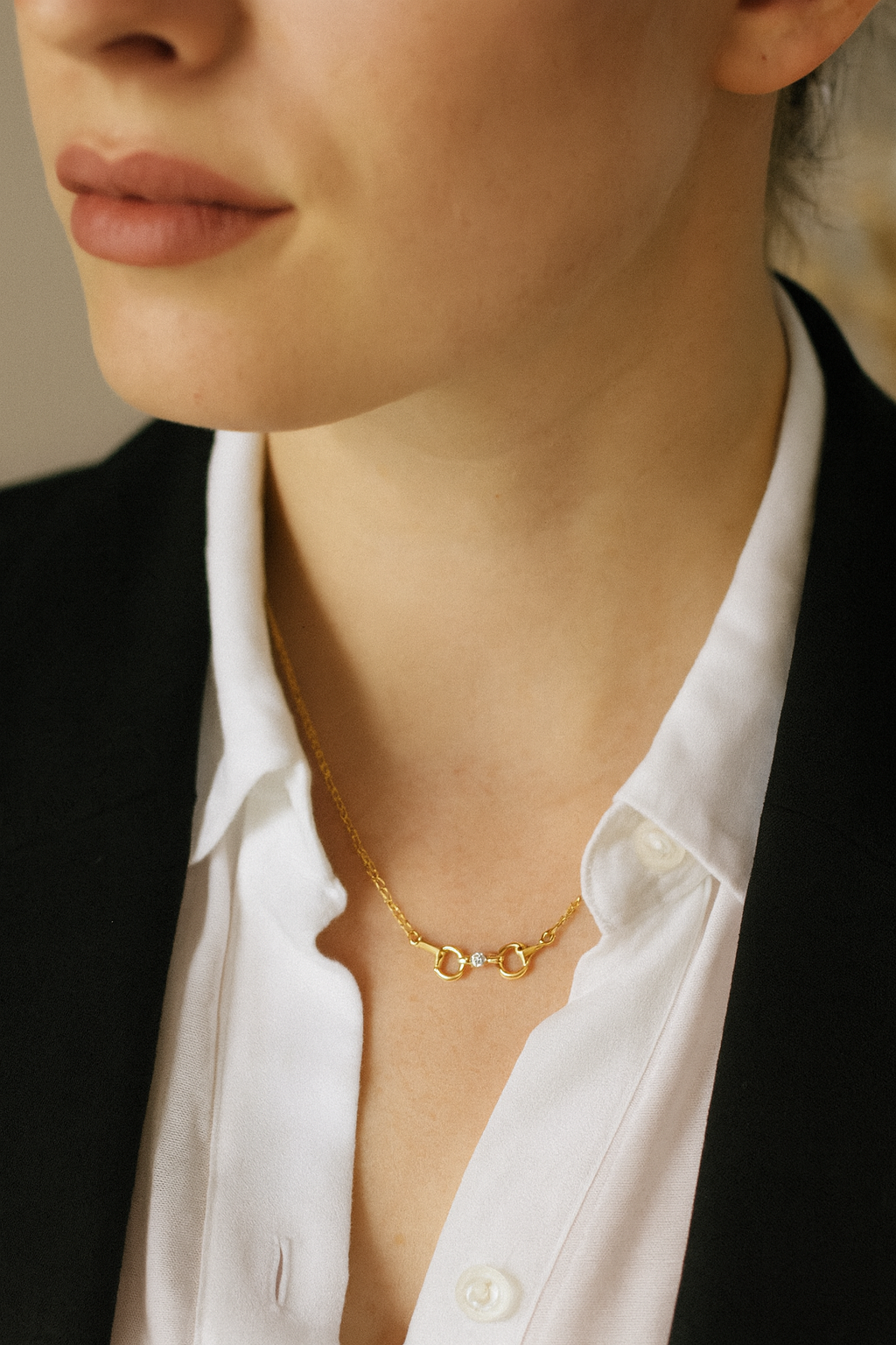 Close-up of a person wearing a gold necklace with a neutral background - equestrian inspired jewelry, horse girl accessory, horseshoe pendant necklace, dainty equestrian jewelry, small gifts for horse lovers