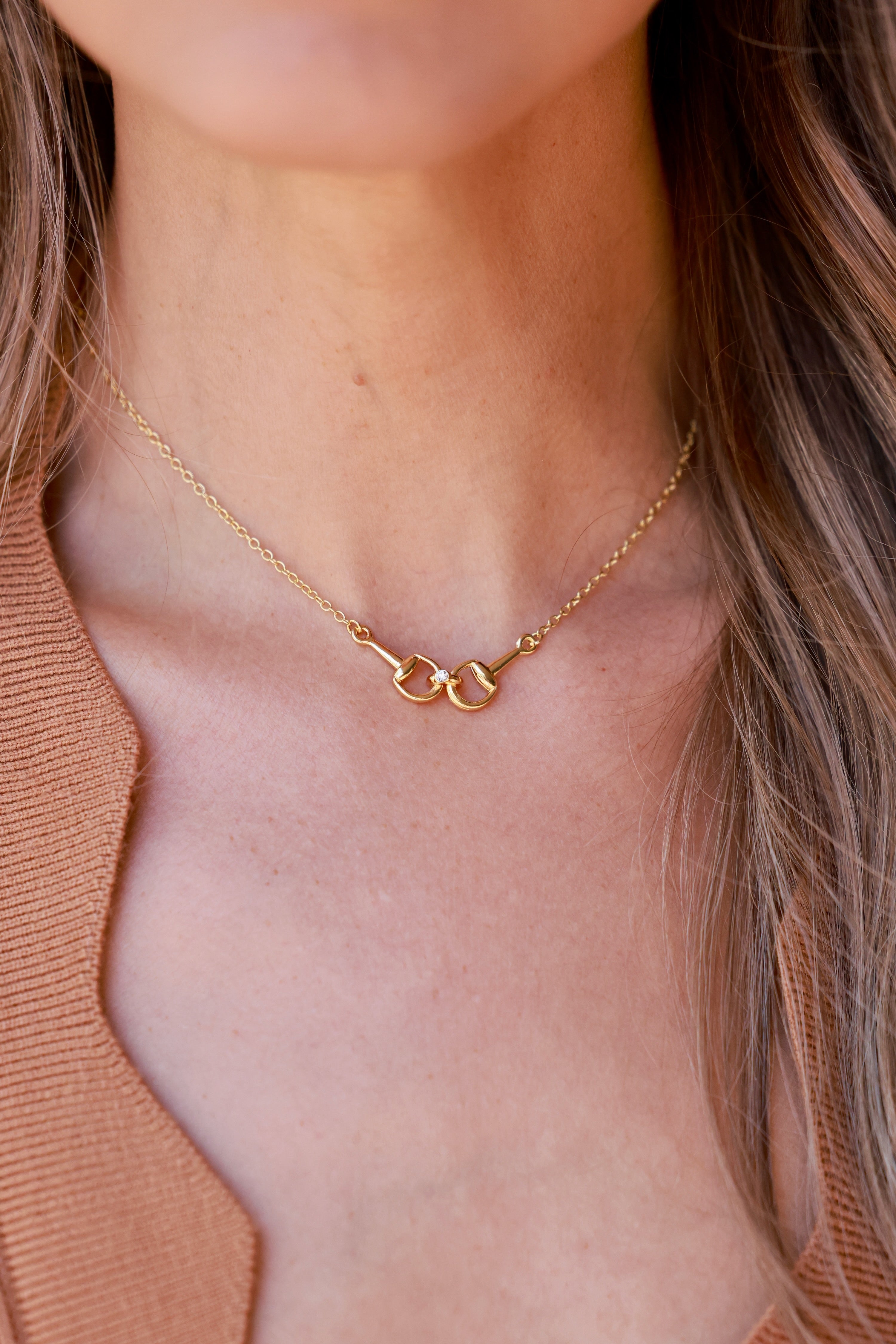 Close-up of a person wearing a gold necklace with a neutral background - equestrian inspired jewelry, horse girl accessory, horseshoe pendant necklace, dainty equestrian jewelry, small gifts for horse lovers