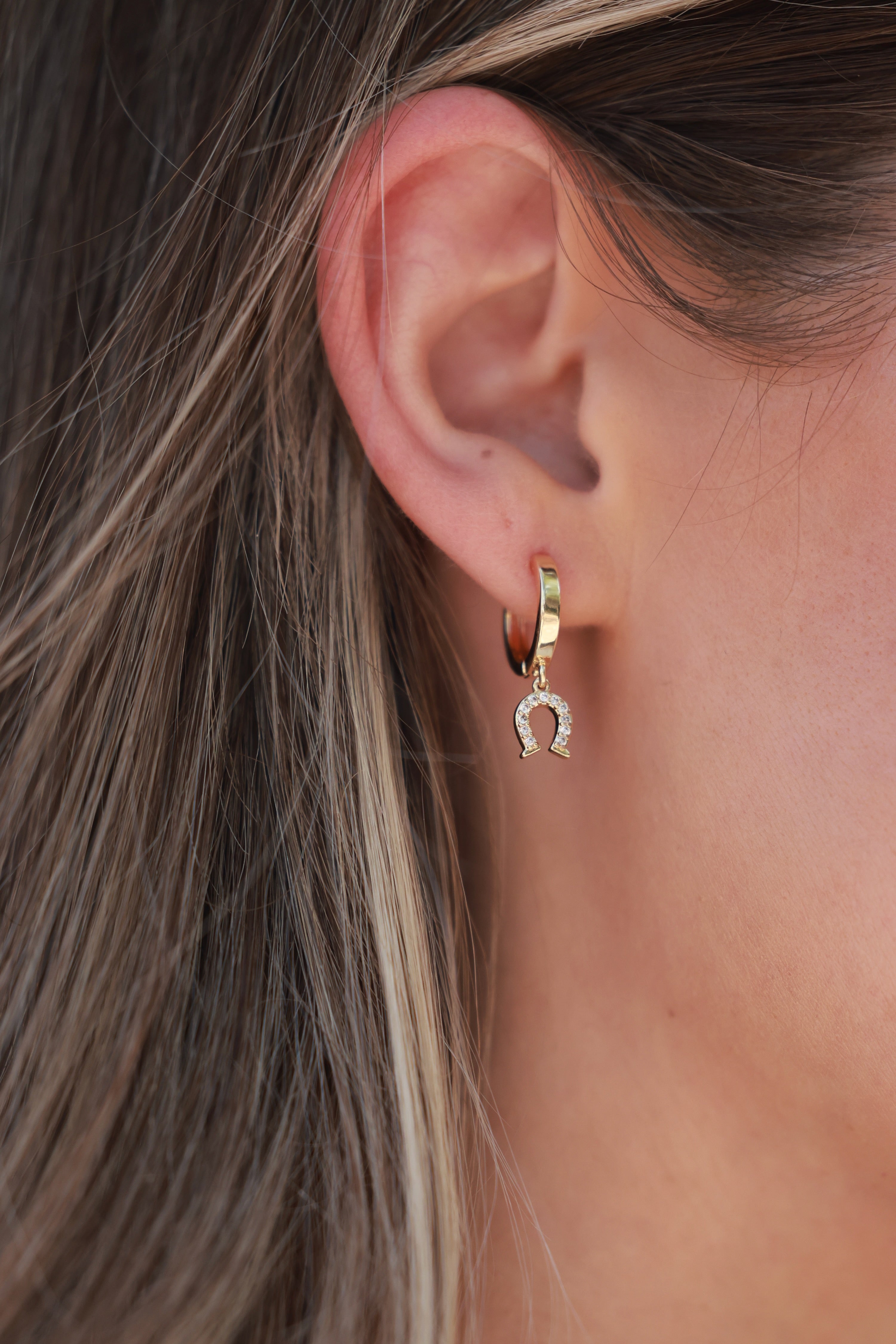 Close-up of an ear wearing a gold hoop earring with a small pendant. - equestrian inspired jewelry, horse themed earrings, dainty equestrian jewelry, horseshoe earrings, small gold hoop earrings, small gifts for horse lovers, horse girl accessories