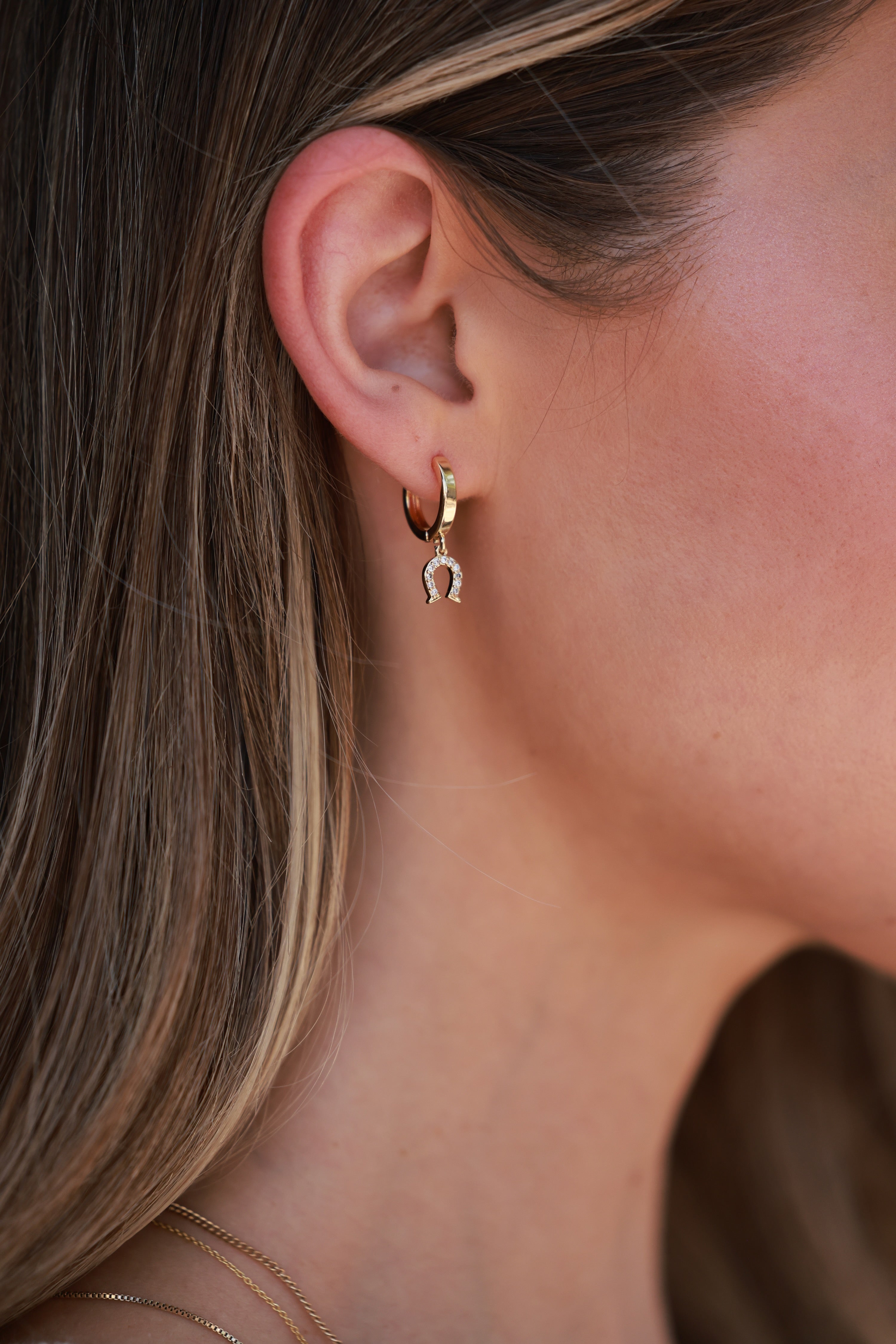 Close-up of a person wearing gold hoop earrings with a blurred - equestrian inspired jewelry, horse themed earrings, dainty equestrian jewelry, horseshoe earrings, small gold hoop earrings, small gifts for horse lovers, horse girl accessoriesbackground