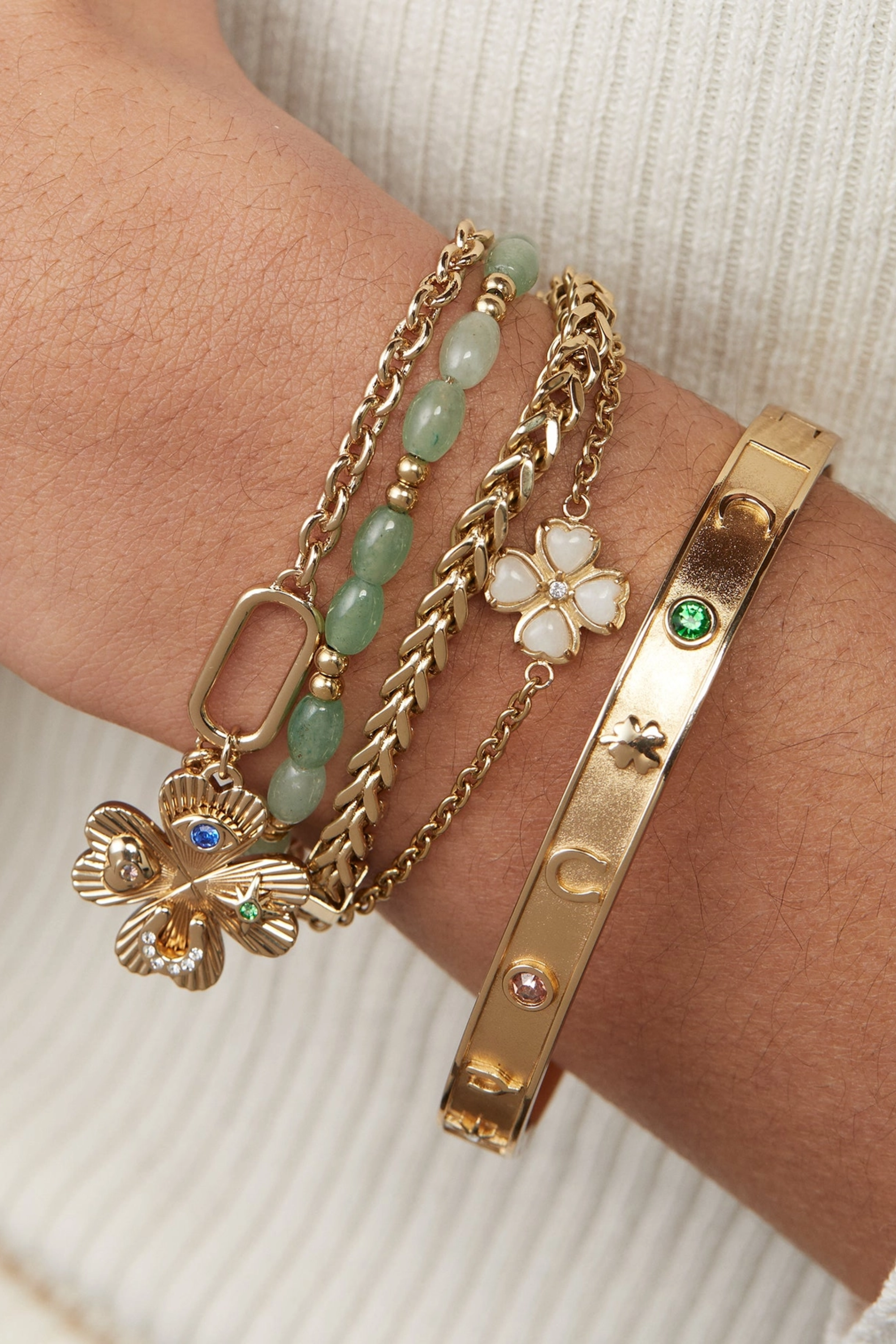 Gold hinge bangle bracelet featuring lucky charm symbols—horseshoe, wishbone, and four-leaf clover—accented with colored crystal details.