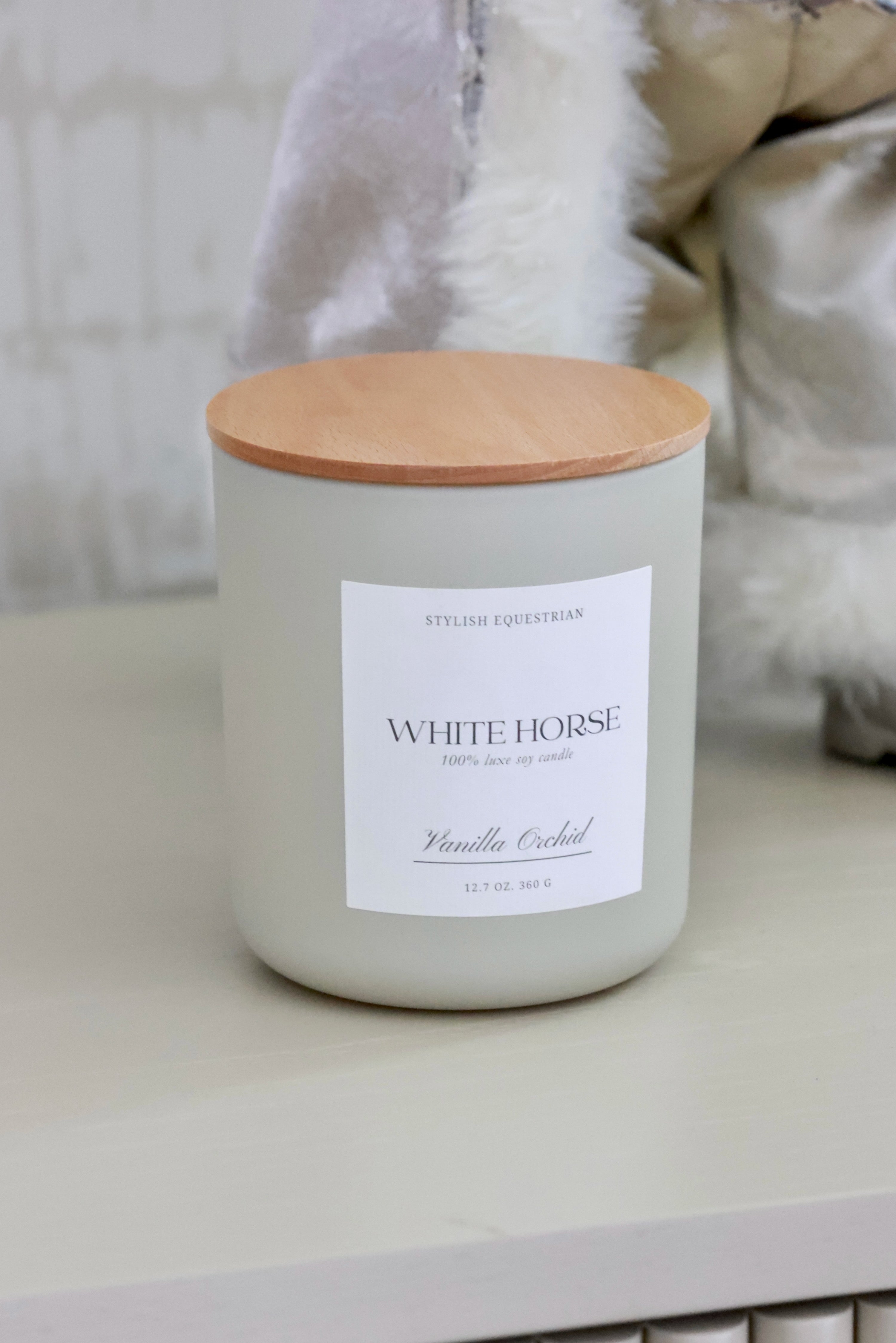 Luxe Signature Candle – White Horse edition, a handmade 100% soy wax candle in a frosted matte glass jar with wooden lid. Features a soothing Vanilla Orchid scent with notes of orange, green leaves, jasmine, sandalwood, and creamy vanilla. Elegant equestrian-inspired home accent with a 60+ hour burn time. Made in the USA. equestrian decor and home accents, horse themed candle, gifts for horse lovers, luxury soy candle, vanilla orchid candle, White Horse candle, equestrian home fragrance