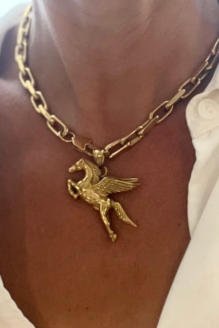 Gold chain necklace with a pegasus pendant on a person wearing a white shirt.