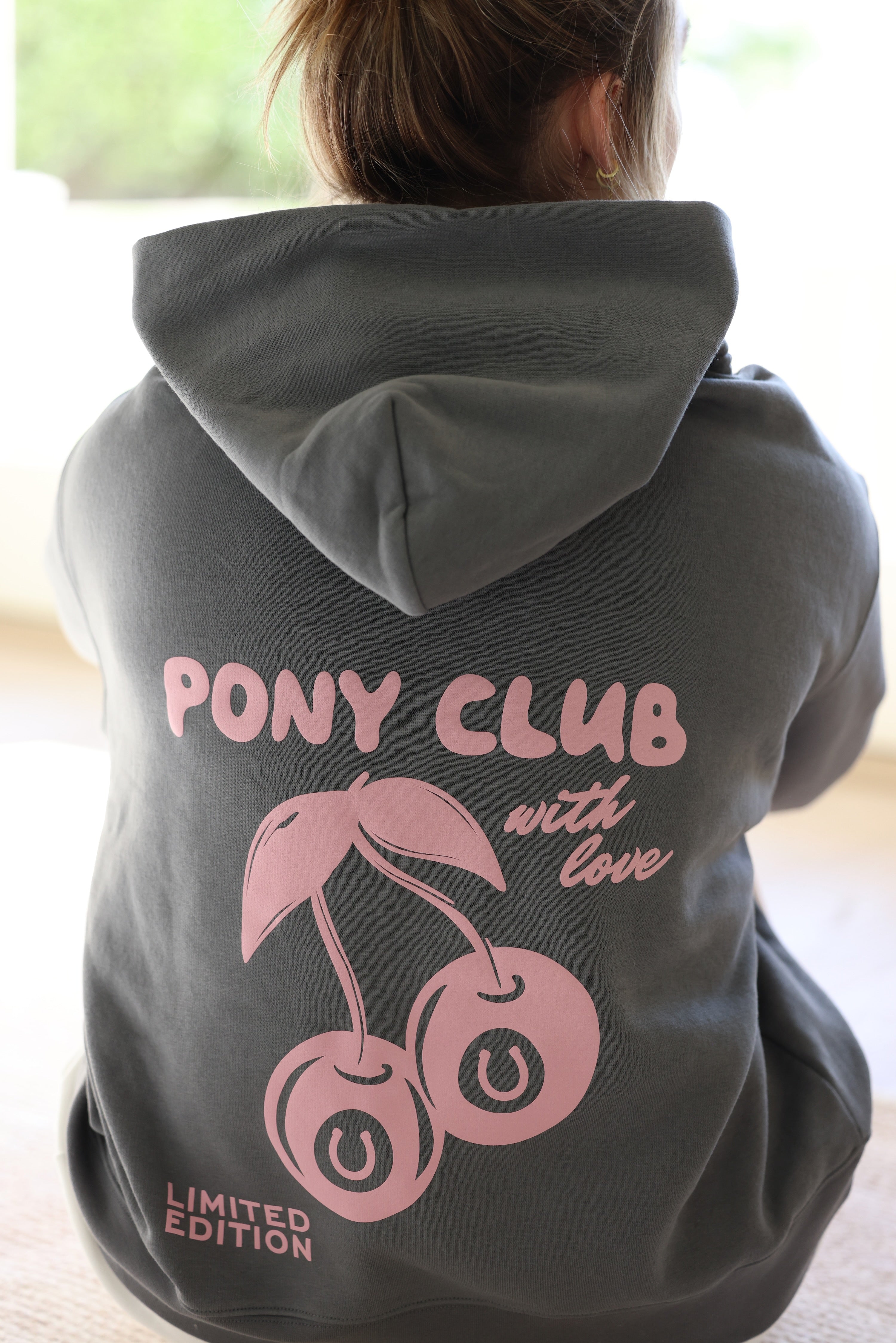 Back view of a person wearing a dark shadow hoodie with pink text "Pony Club with love" and cherries graphic. "Limited Edition" is printed at the bottom.