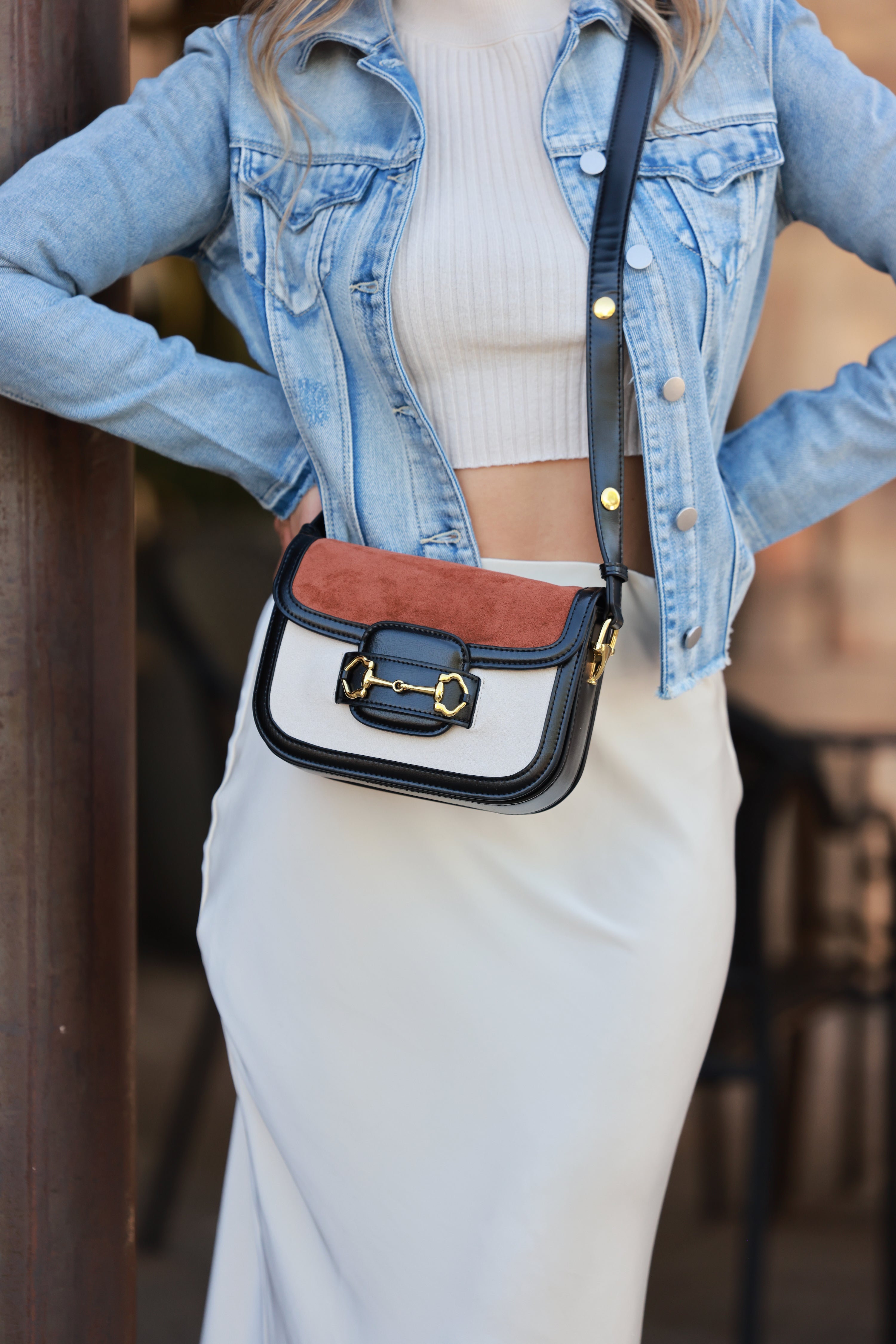 Person wearing a denim jacket and white pants with a black and white handbag featuring a red interior. equestrian accessory, horse bit handbag, horse themed accessory, gifts for horse lovers