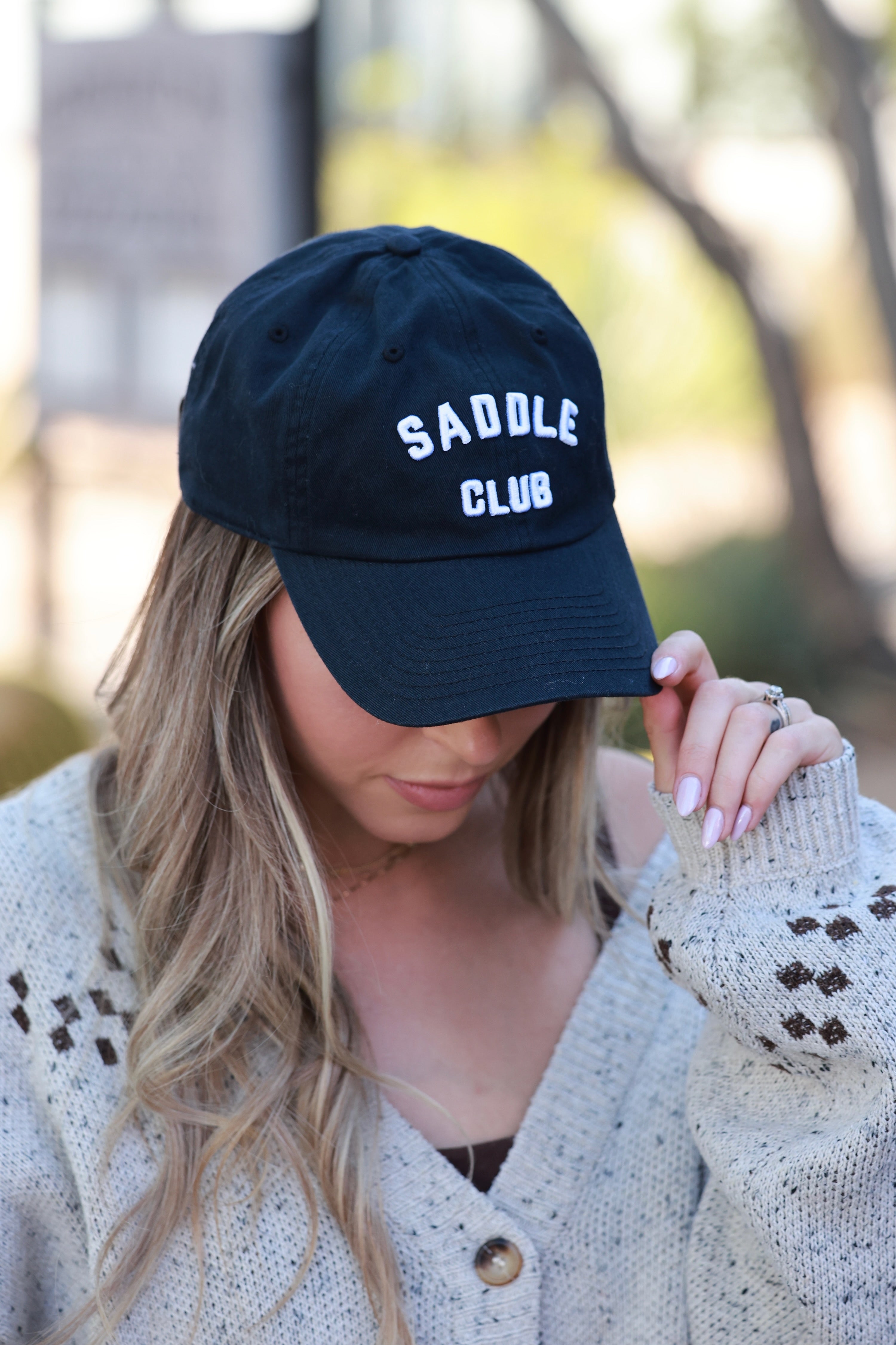 Person wearing a black cap with 'Saddle Club' text, outdoors. - equestrian accessory, horse riding gear, horse girl baseball cap, horse show hat