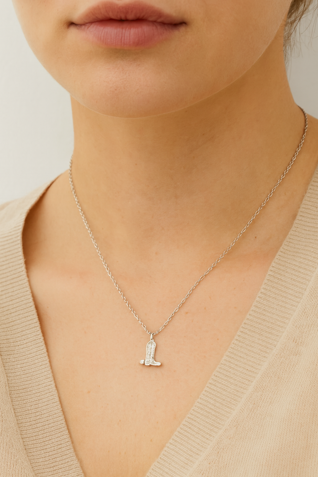 Necklace with a boot pendant worn by a person in a beige sweater.