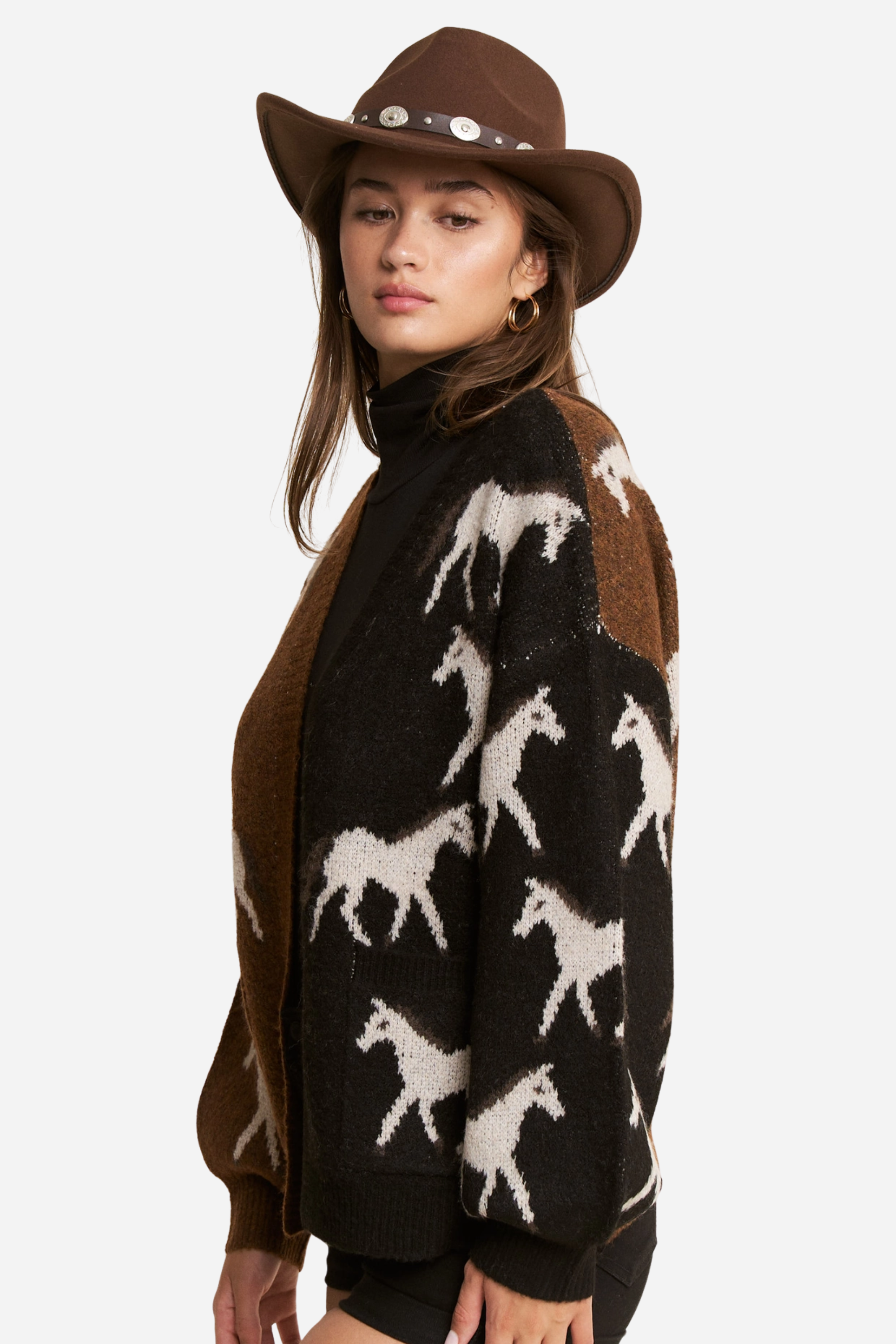 Person wearing a two-tone knit horse cardigan in brown and black, featuring white prancing horse patterns on the front and back. This soft, stretchy equestrian sweater includes long sleeves, cuffed trim, and pockets, perfect for horse girl apparel and western-inspired outfits.