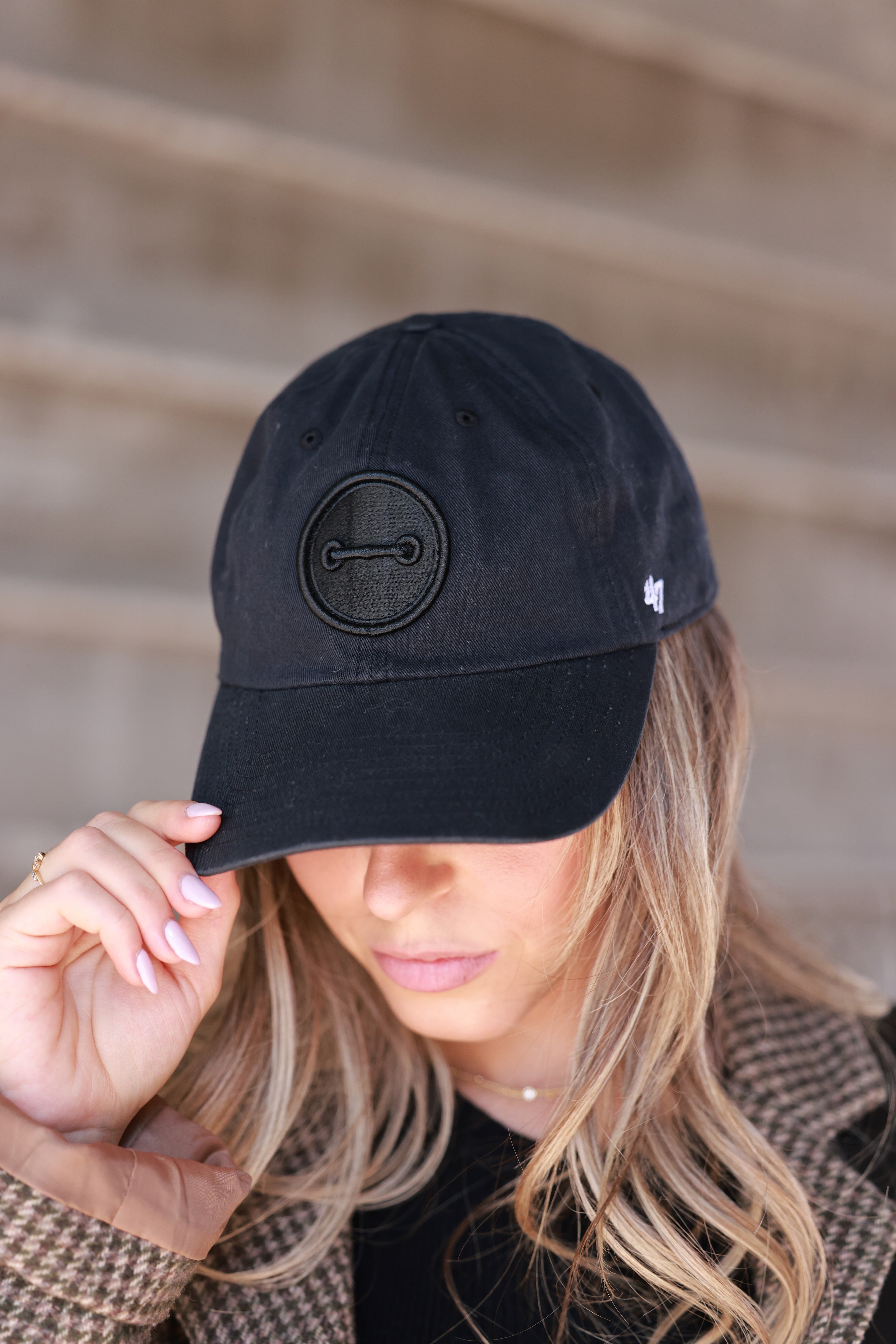 Person wearing a black cap with a logo, blurred background - horse bit hat, equestrian headwear, horse girl accessories, casual riding gear, horse riding accessories, baseball cap