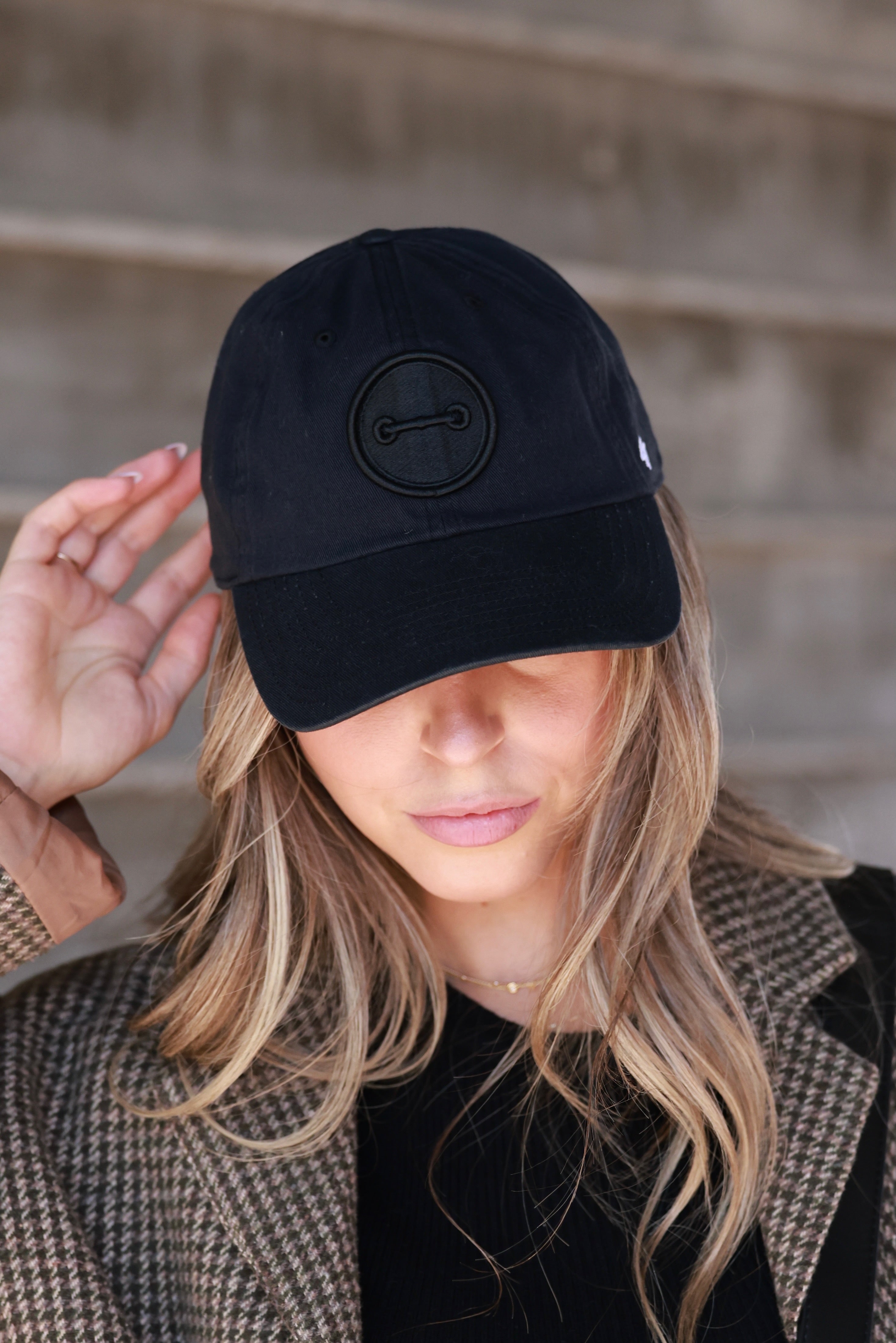Person wearing a black cap with a bit logo against a neutral background - horse bit hat, equestrian headwear, horse girl accessories, casual riding gear, horse riding accessories, baseball cap