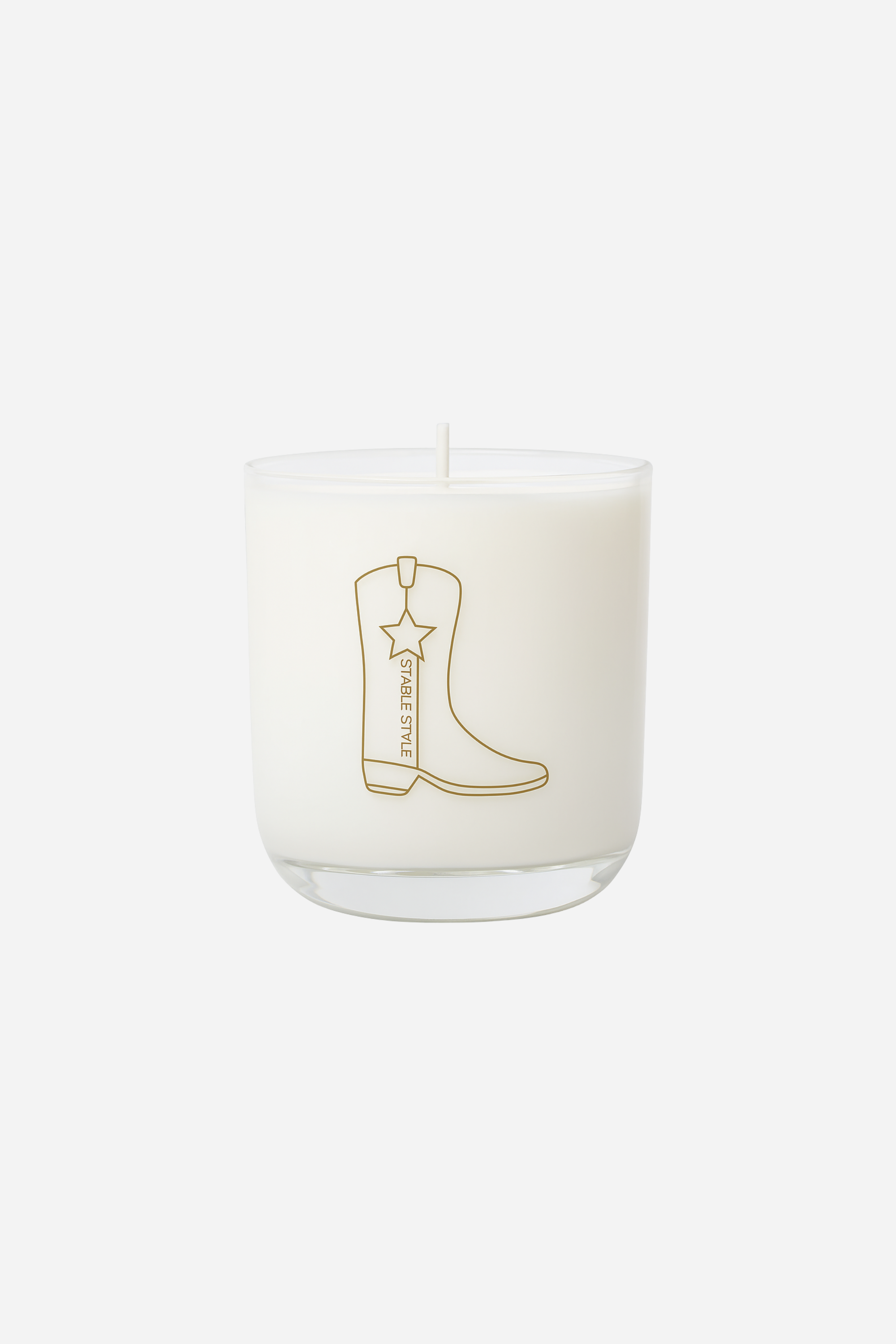 10-ounce soy wax candle from the Icons Collection by Stable Style, hand-poured into a clear glass vessel with a rounded base and gold accents. Fragrance opens with tobacco flower, anise, nutmeg, clove, and ginger, with warm mid notes of vanilla, tonka bean, and cocoa, and a rich base of amber, agarwood, and sweet fruit. Elegant packaging comes in a gold-foil wrapped paper tube, offering 60+ hours of burn time.