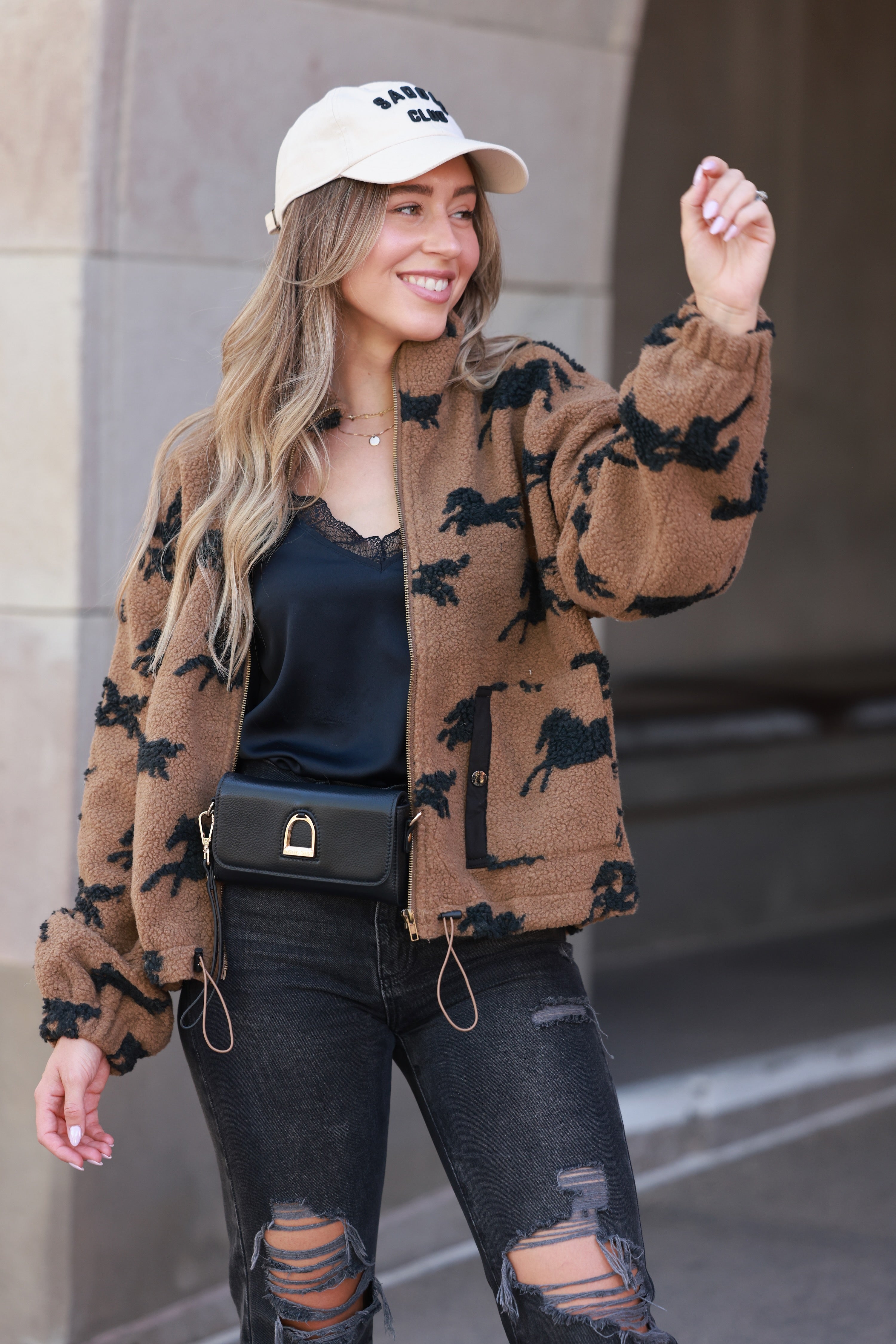 Woman wearing a patterned cardigan, black top, and ripped jeans with a blurred background - equestrian sherpa jacket, equestrian jacket, horse print jacket, equestrian outerwear