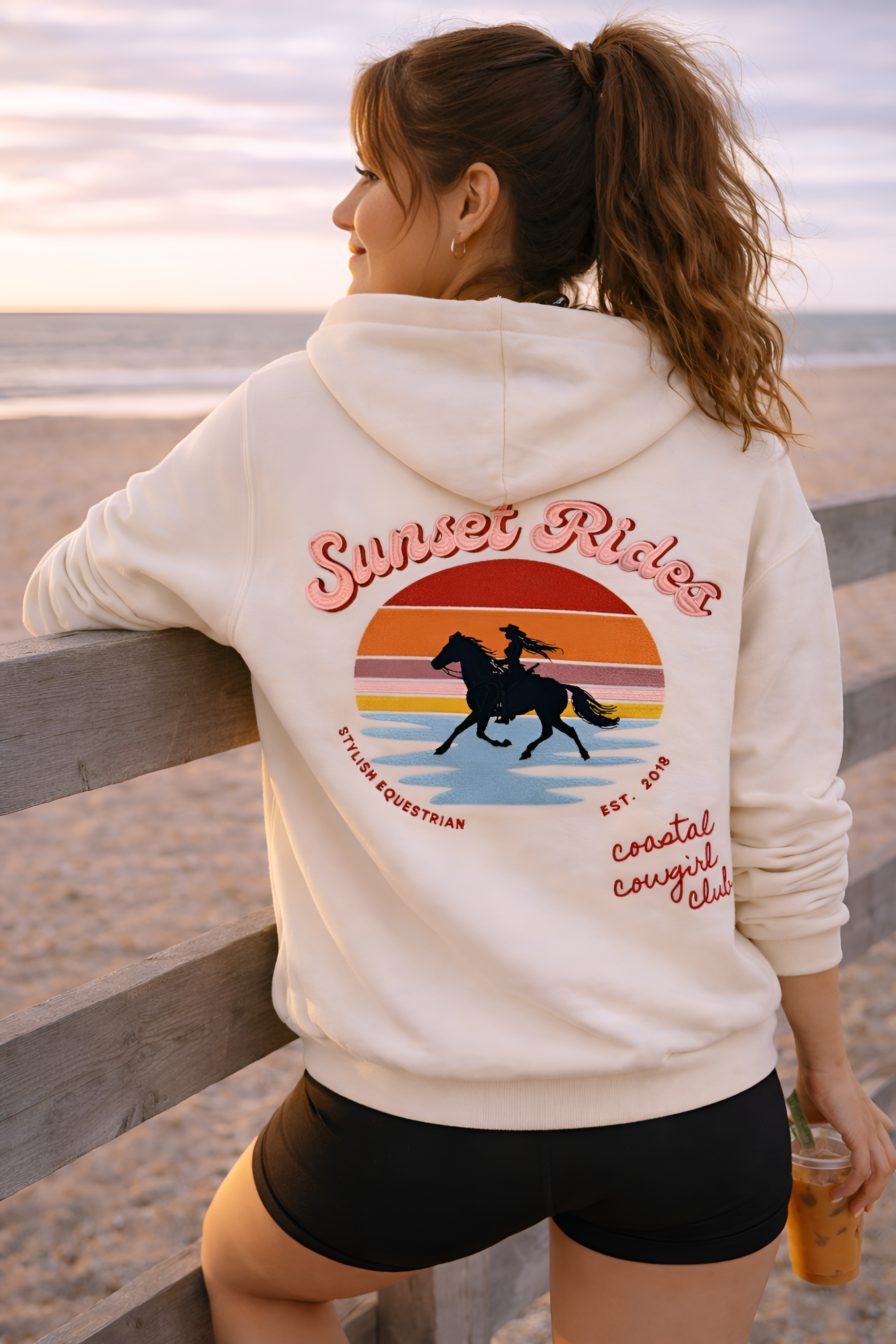 Woman wearing a 'Sunset Rides' hoodie on a beach