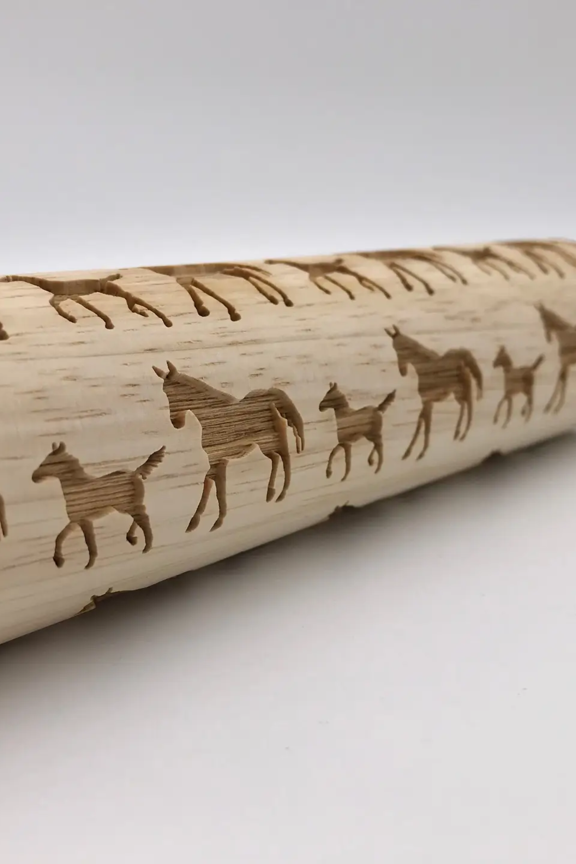 A Horses Embossed Rolling Pin featuring a detailed horse pattern carved into the wood, resting on a kitchen surface beside embossed cookies and baking tools. The intricate design showcases elegant horse motifs that create artistic imprints on dough, fondant, or clay—highlighting the pin’s versatility for baking and crafting.