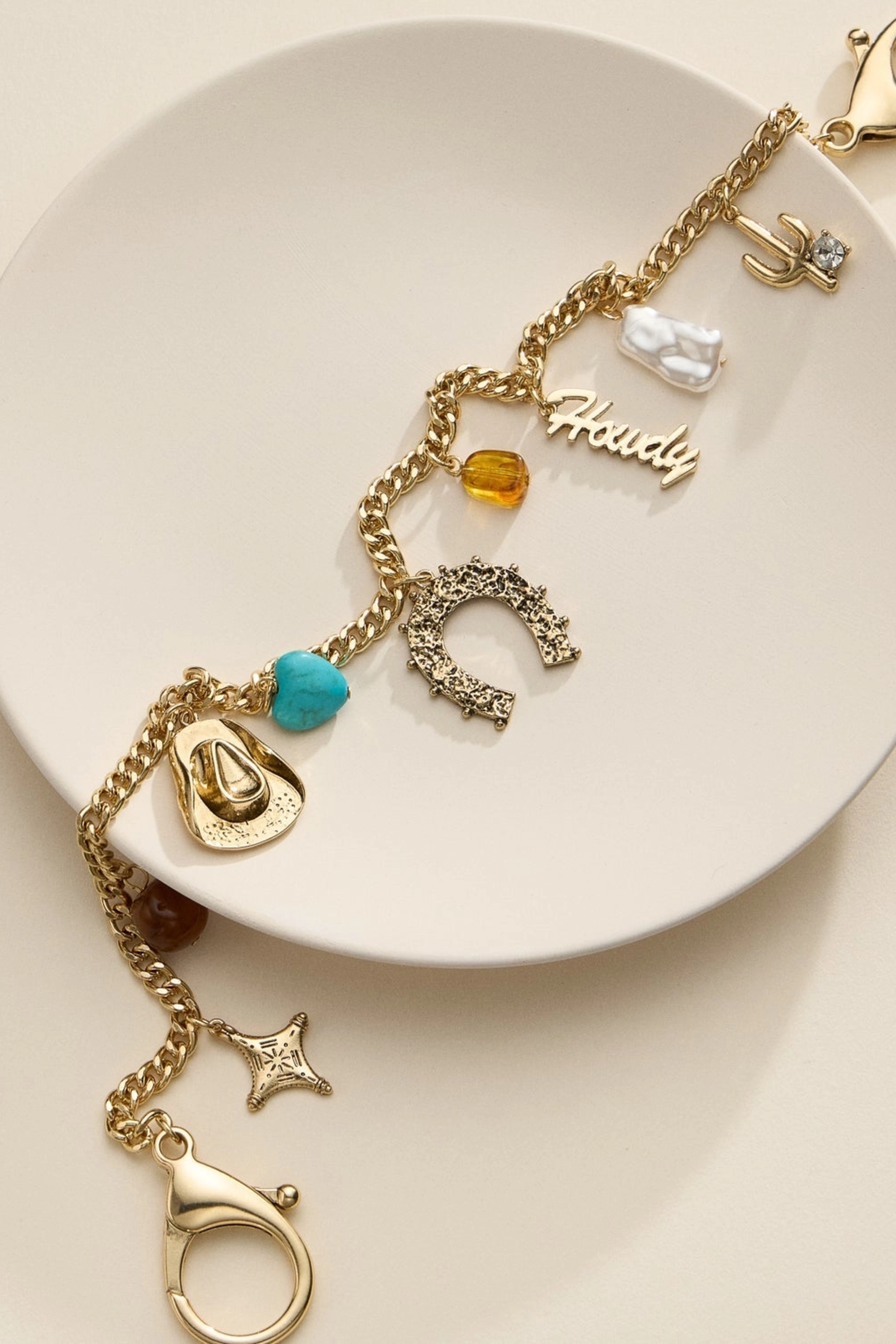 Gold-tone western bag charm chain adorned with a horseshoe, cowboy hat, and turquoise heart charms, designed to add equestrian flair to handbags.