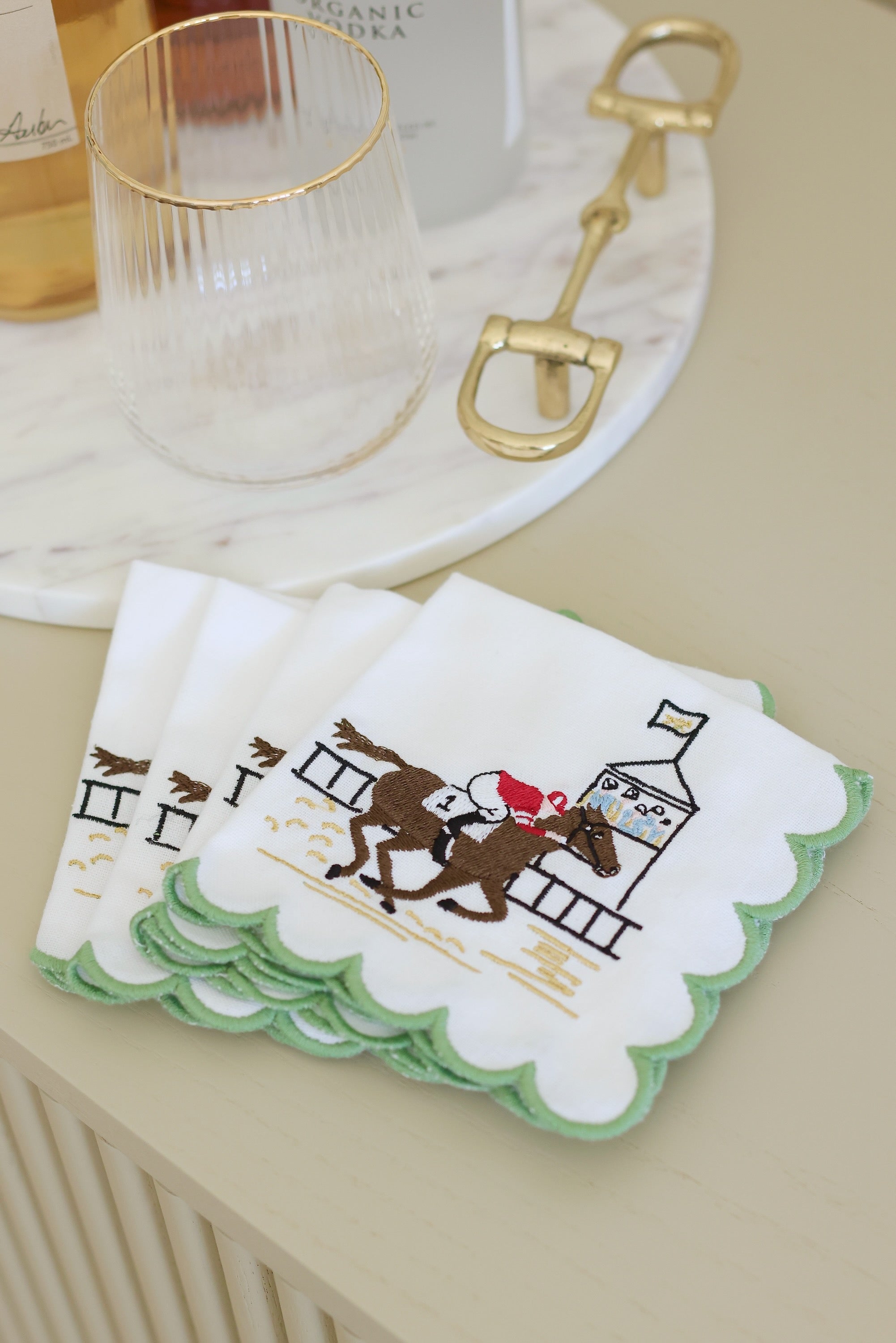 Pomegranate At The Finish Cocktail Napkin Set A toast to the thrill of the track! Our At the Finish Embroidered Cocktail Napkins bring race day excitement to every sip. Featuring a spirited racehorse and jockey charging past the finish line, these embroidered white cotton napkins with a green scalloped edge are a festive nod to the sport of kings—and the queens who throw a fabulous party. 