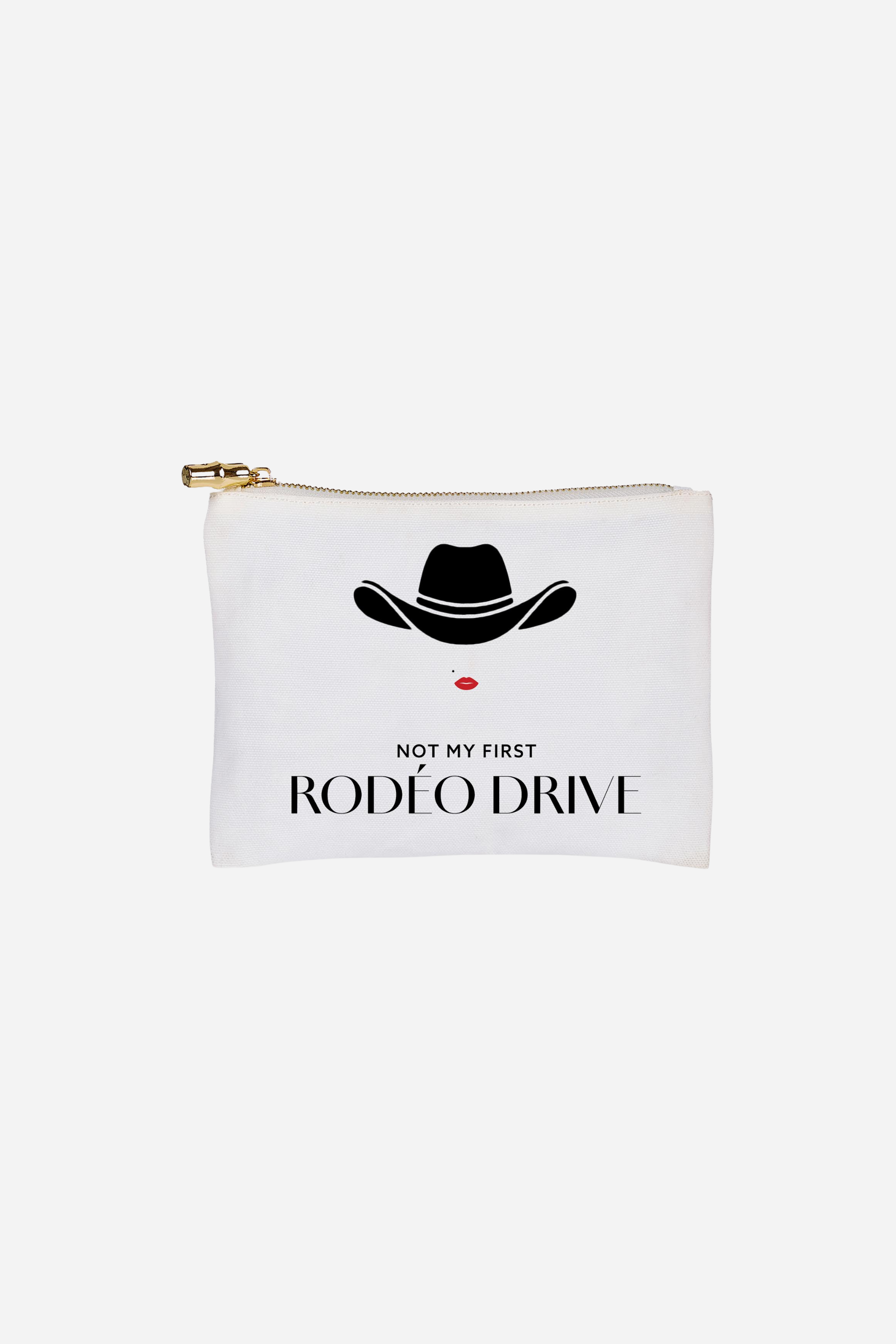 Toss Designs Rodéo Drive Flat Zip Pouch | White pouch with a black cowboy hat, red lips, and the text "NOT MY FIRST RODÉO DRIVE." | Rodeo Drive pouch, Western glam clutch, cowboy hat makeup bag, trendy statement accessory, red lips graphic pouch, modern cowgirl gift, chic fashion zipper pouch.